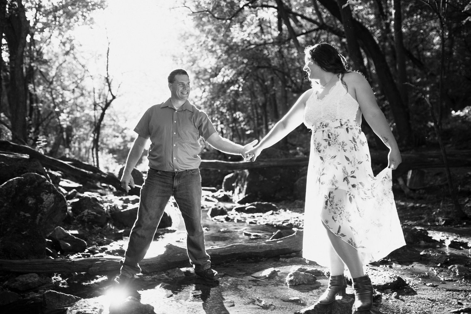 Couple holding hands while balancing on rocks in black and white photo.