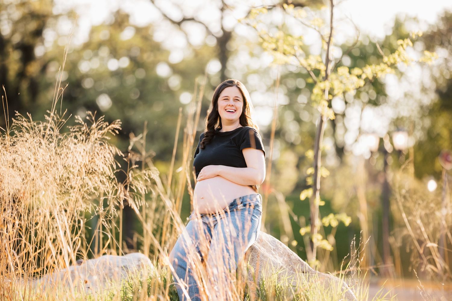 Person poses in field during golden hour maternity photoshoot.