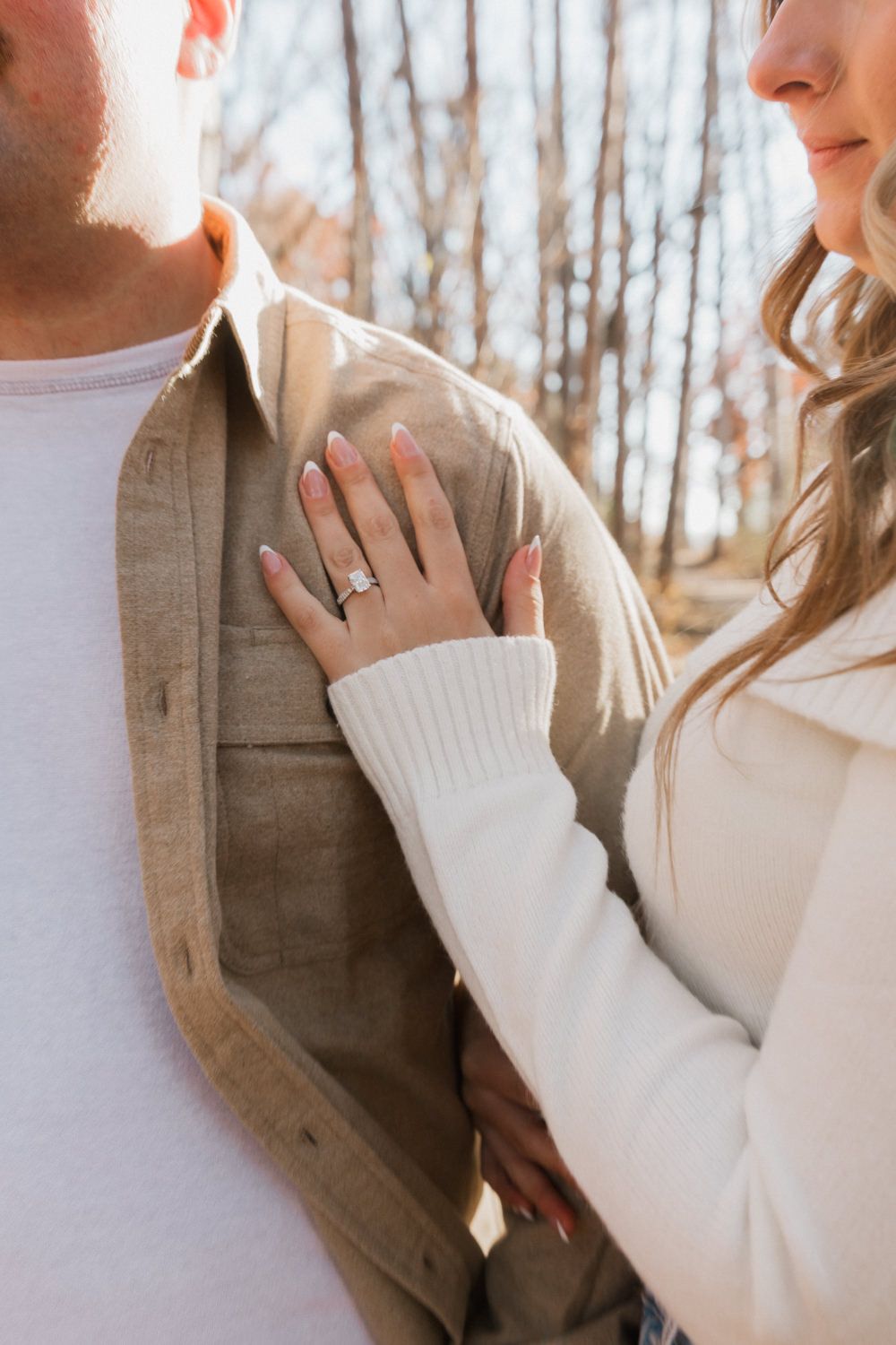 Close-up shot of a couple in white and tan clothing sharing an intimate moment in a wooded setting.