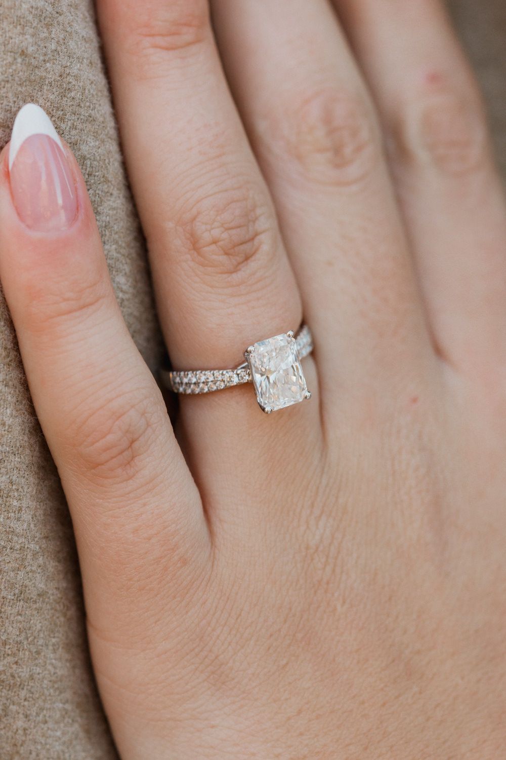 Close-up shot of an elegant diamond engagement ring on a hand against a neutral background.
