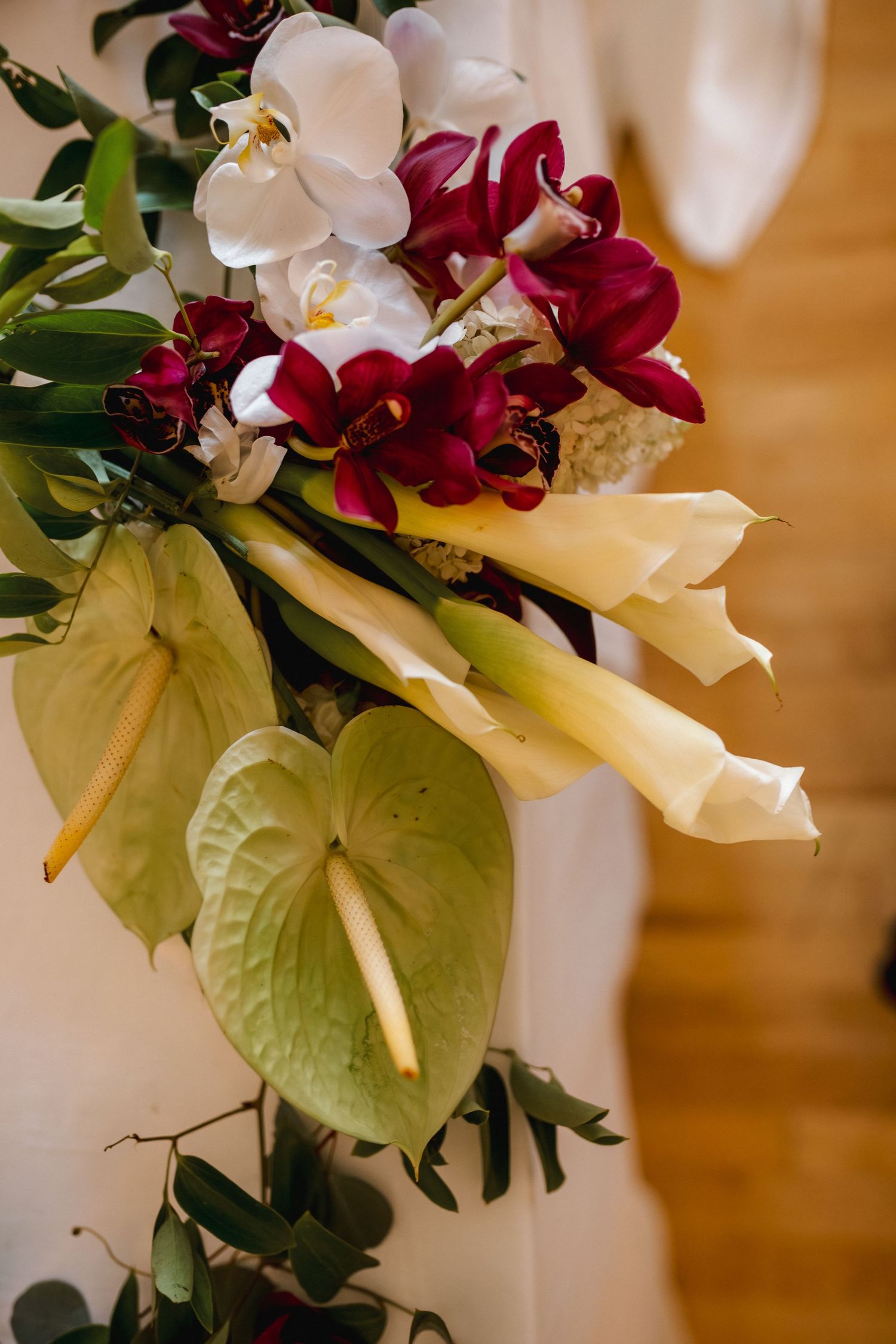 Elegant wedding floral arrangement featuring white orchids, burgundy cymbidium orchids, calla lilies, and green anthurium.