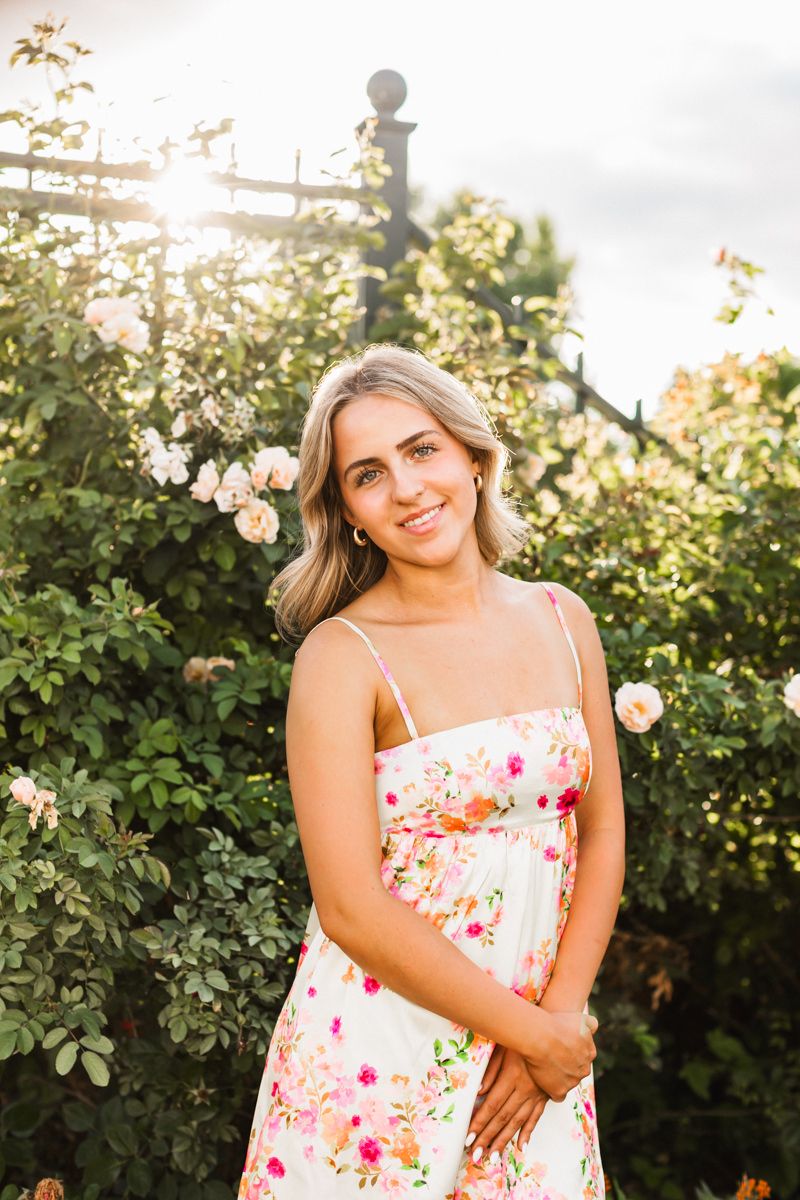 Garden photography with floral dress against blooming rose bushes in evening light.