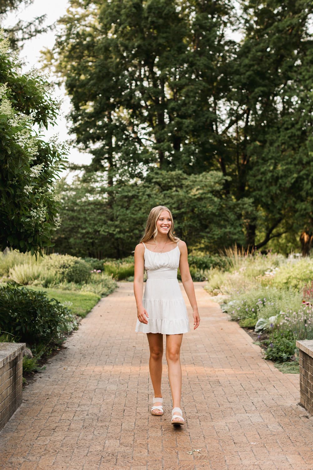 A white summer dress and sandals on a brick pathway surrounded by lush garden landscaping.