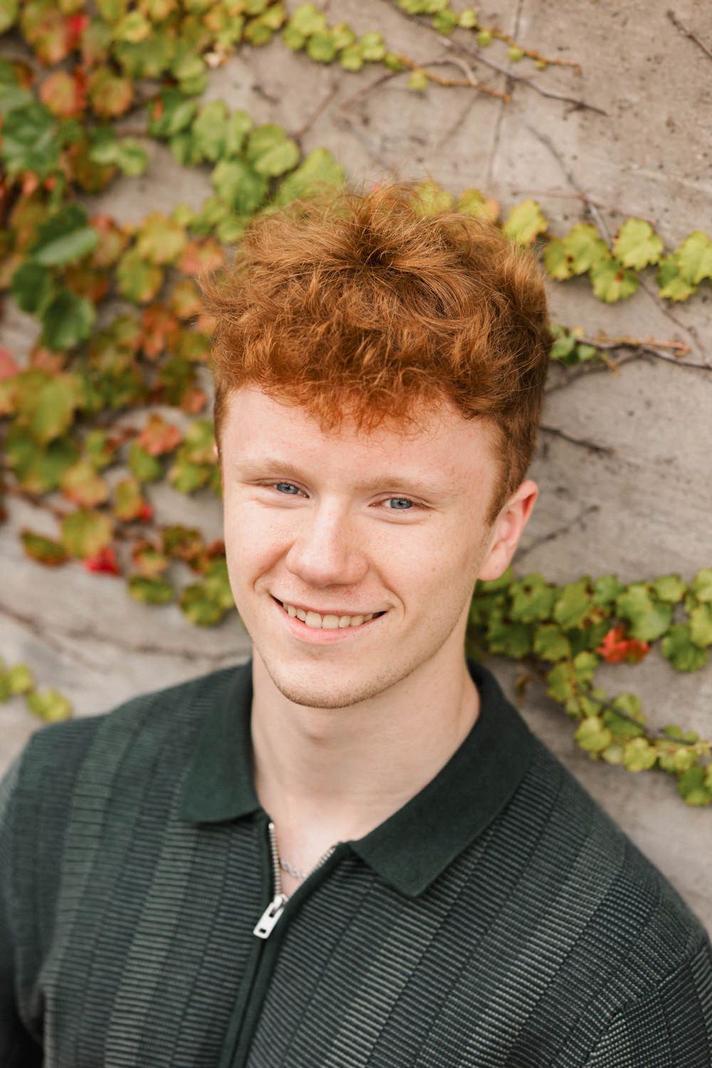 Portrait shot with ivy covered wall background showcasing relaxed expression.
