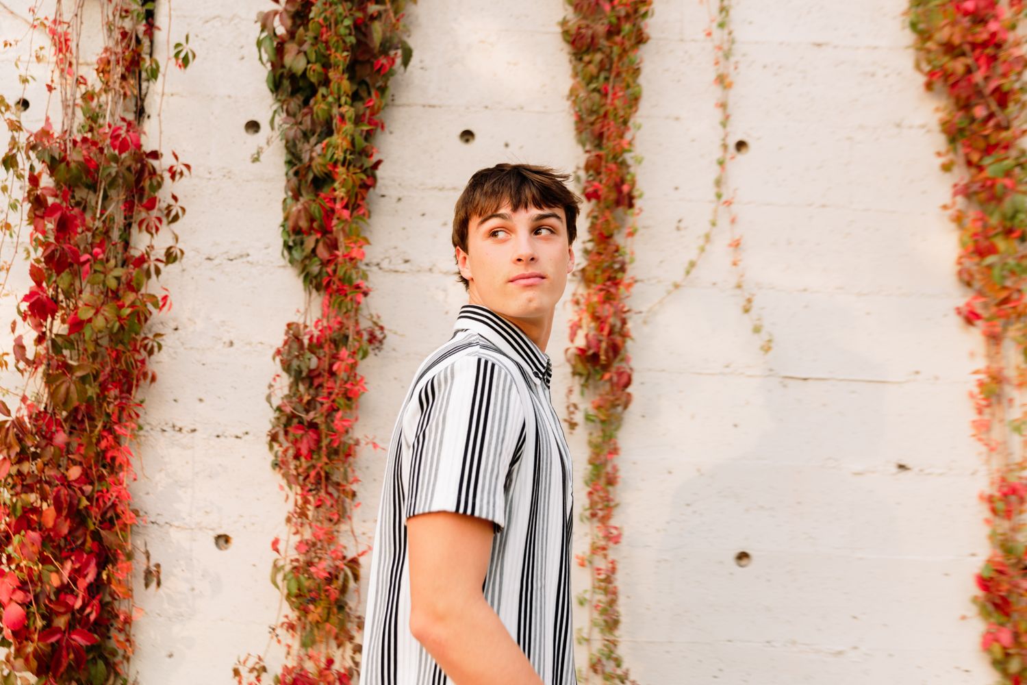 Person standing against white wall with vibrant red and orange autumn ivy vines.