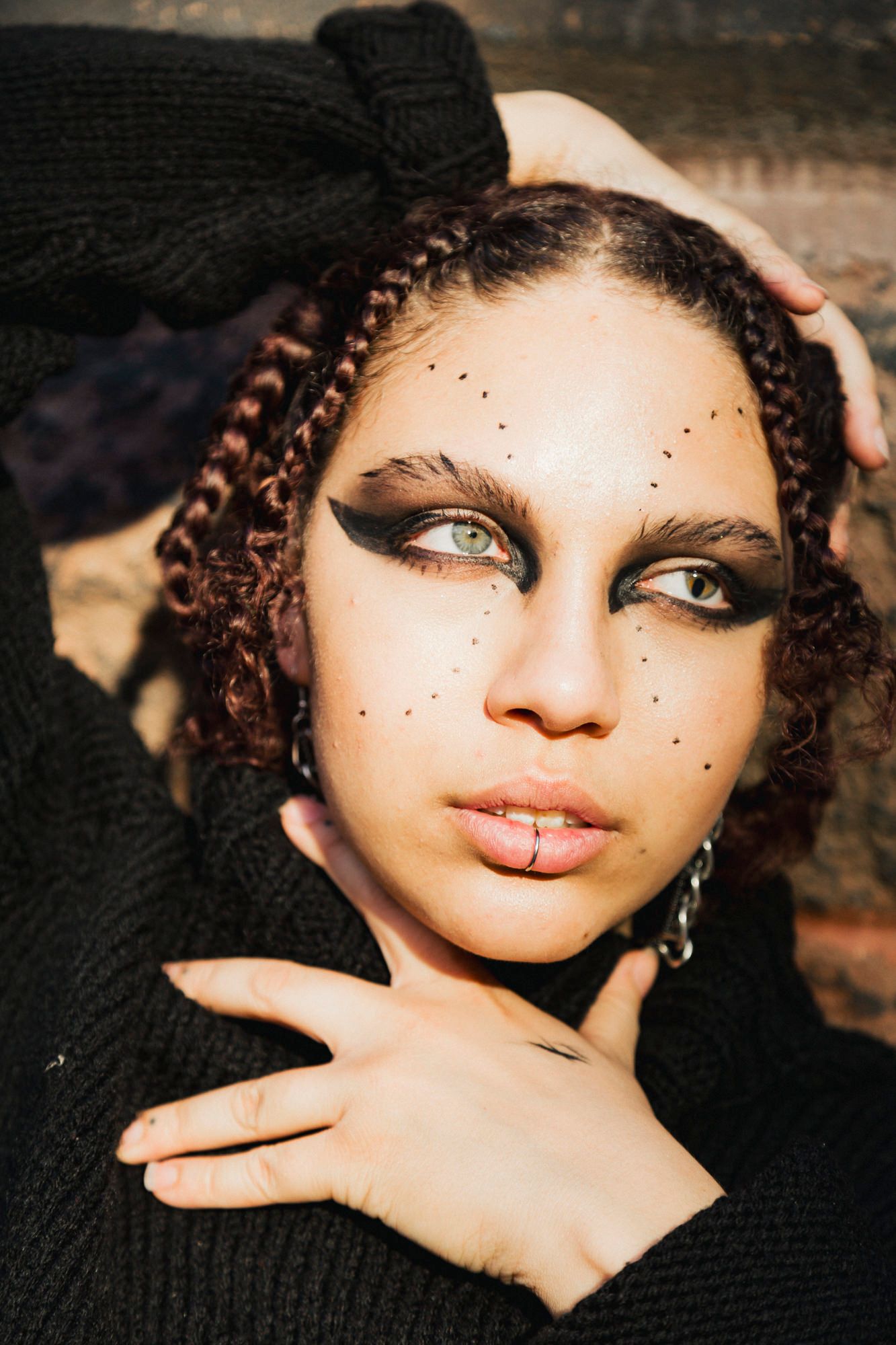 Artistic beauty portrait featuring dramatic eye makeup with glitter dots and braided hair against a dark background.