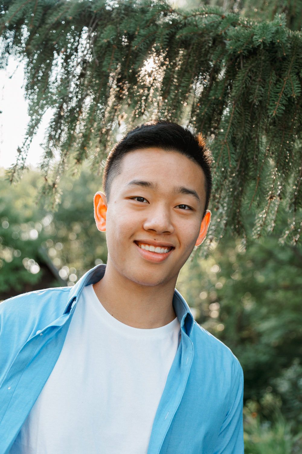 Portrait outdoors featuring a light blue button-up shirt against a natural green background with trees.