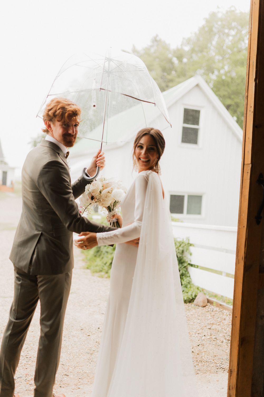Couple shares a private moment behind white umbrellas on a rainy wedding day.