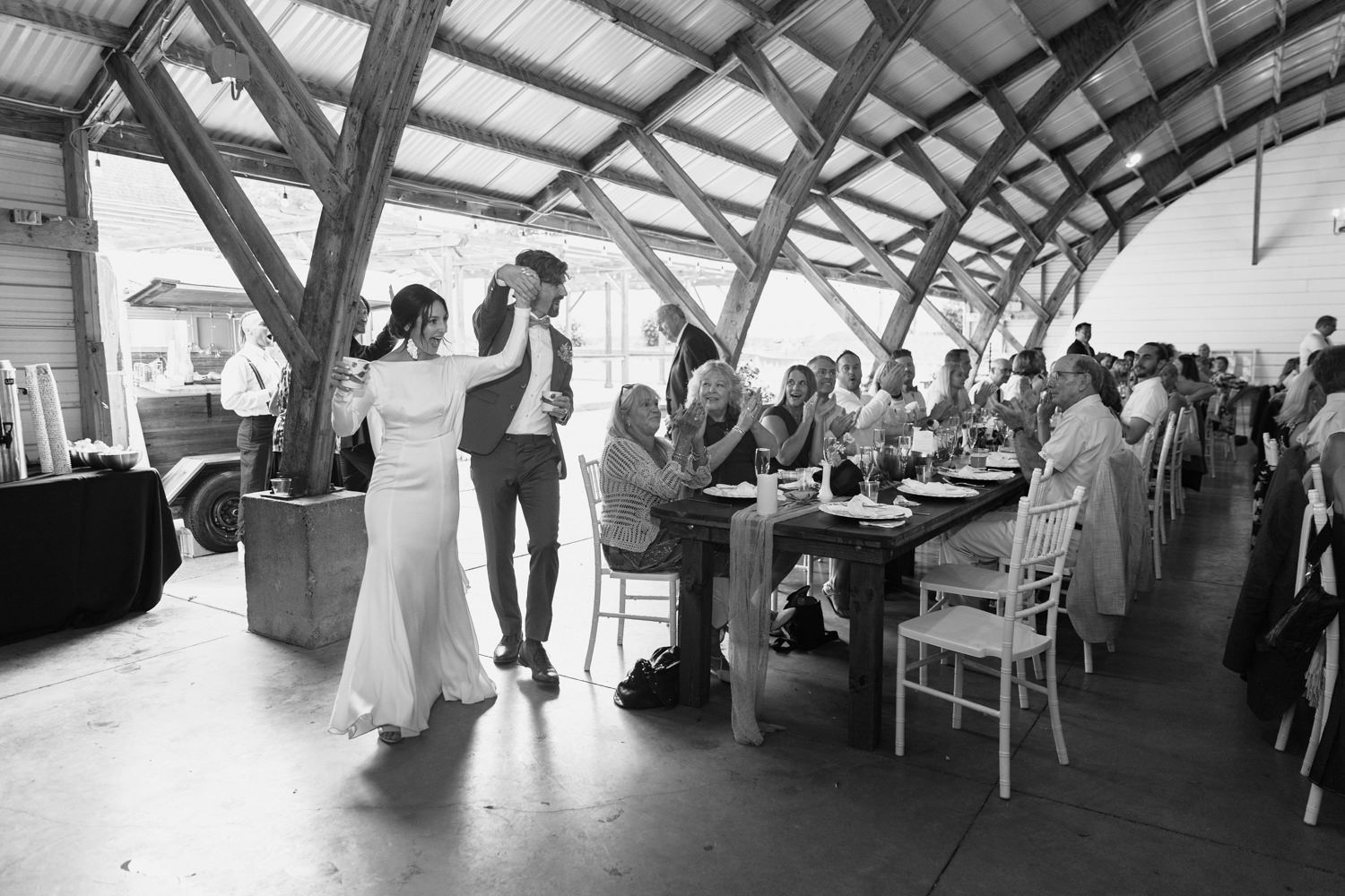 A panoramic view of a wedding reception venue with guests seated at tables under a covered outdoor pavilion.