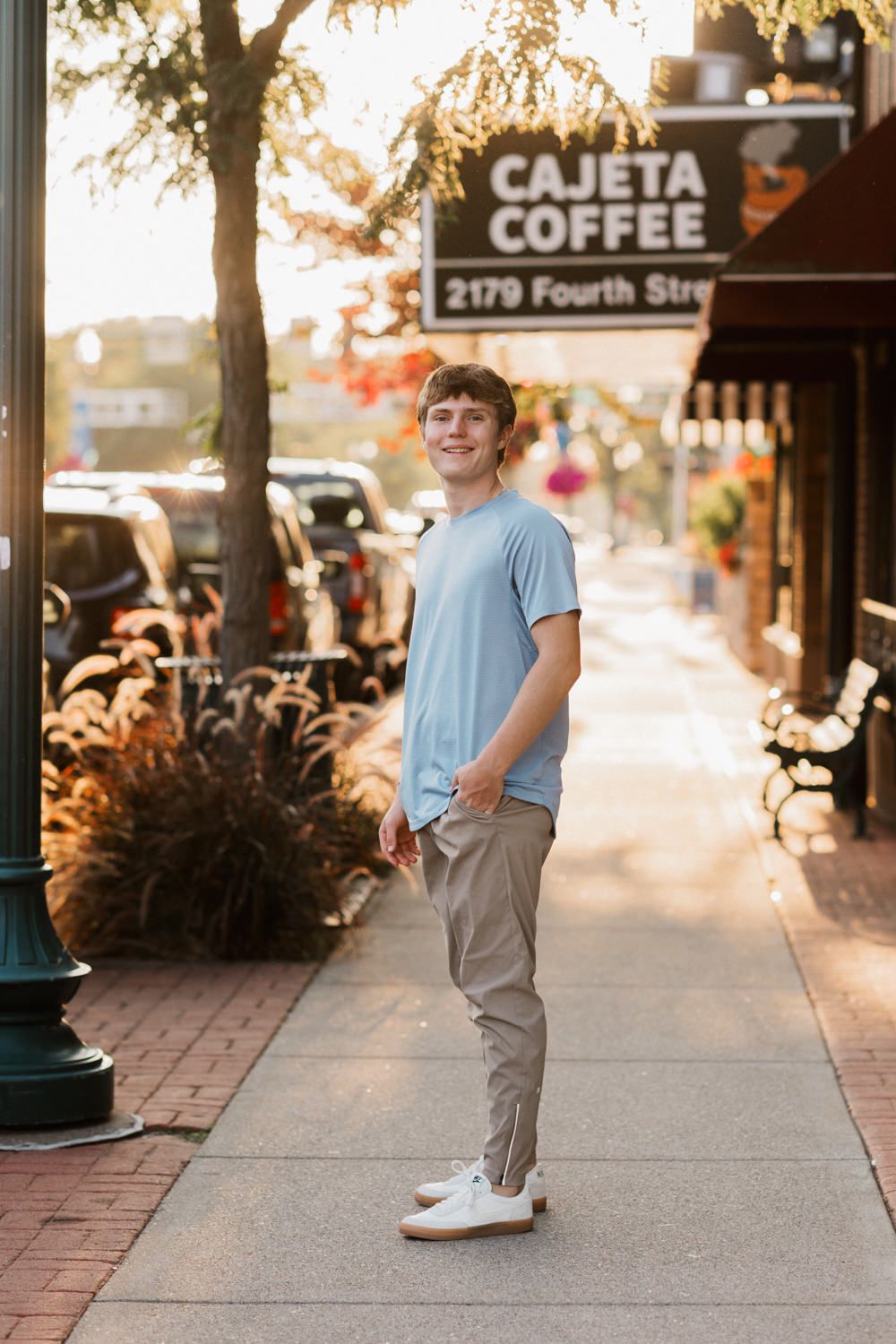 Person in light blue shirt and khakis stands on sidewalk outside Cajeta Coffee shop on a sunny day.