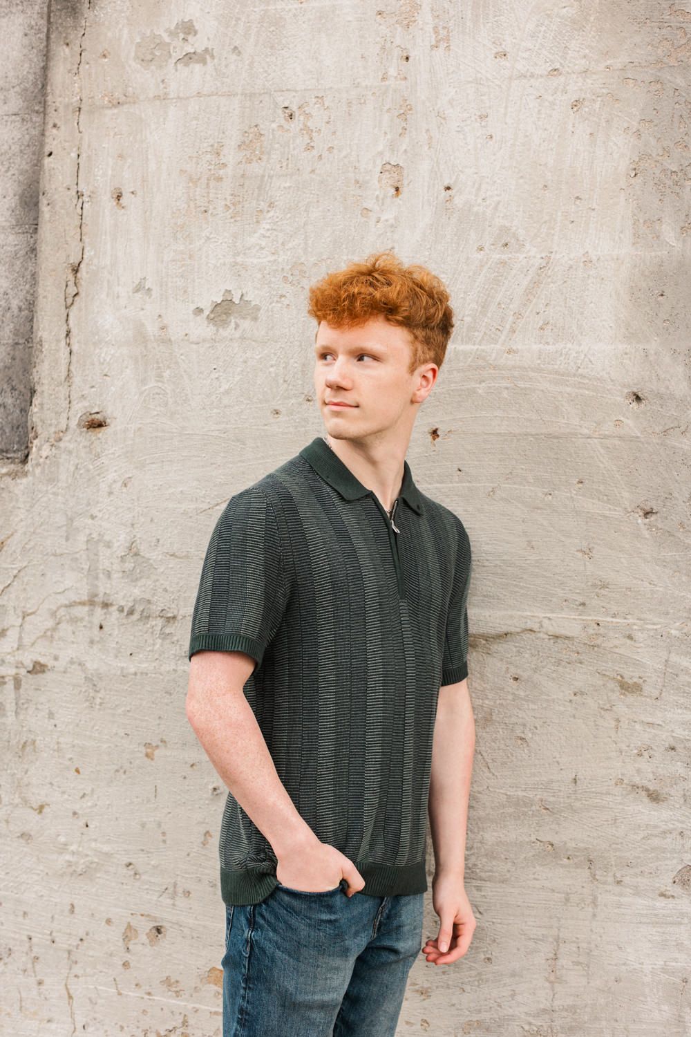 Person in dark polo shirt standing against concrete wall in casual urban portrait.