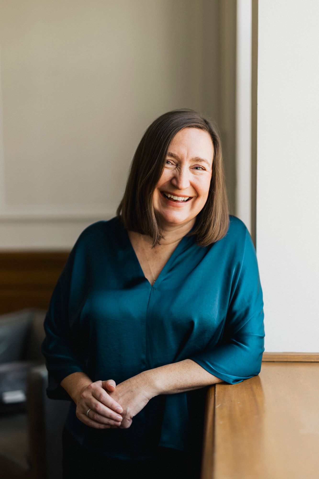 Professional portrait of person in teal blouse smiling by window.