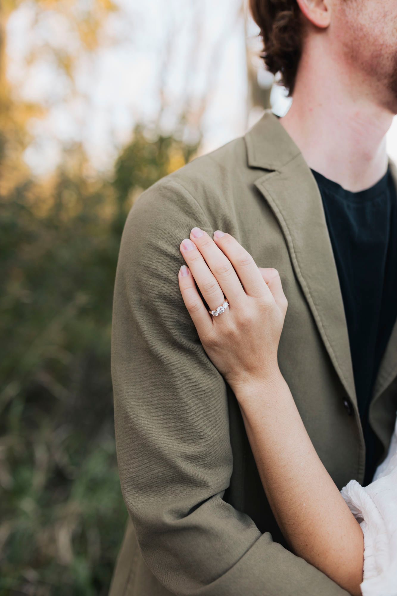 Close up shot of an engagement ring as a couple embraces outdoors.