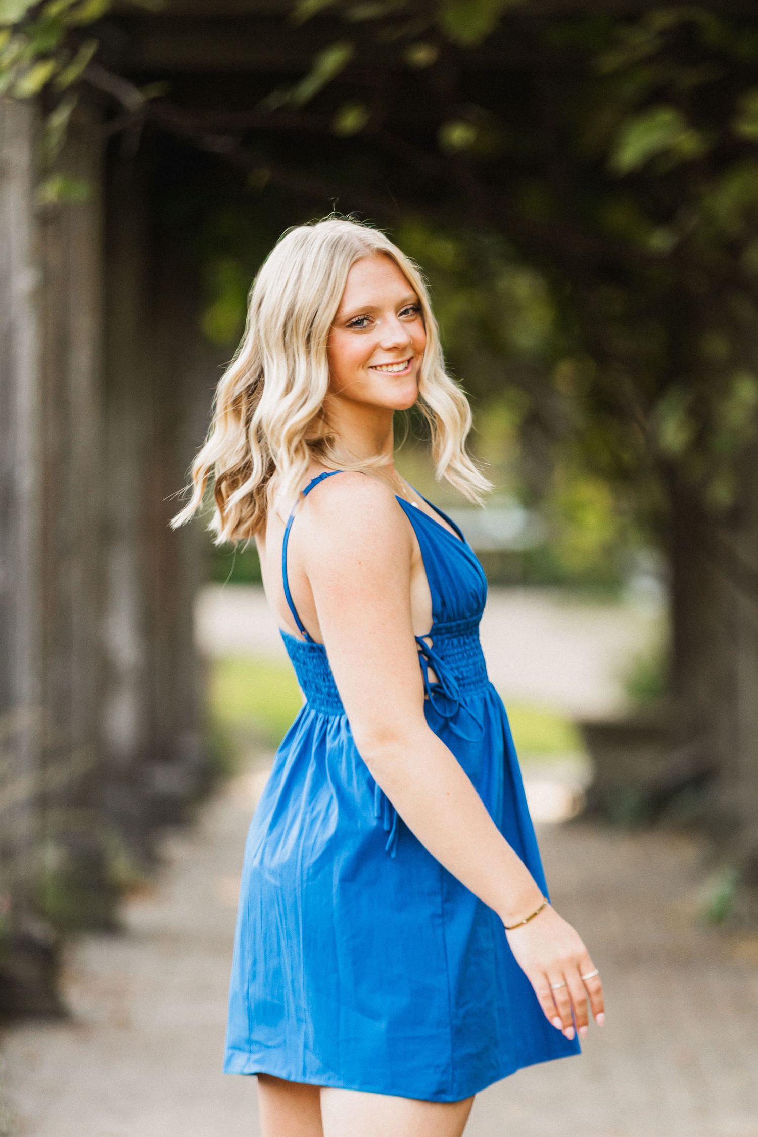 Woman in bright blue sleeveless top smiles and twirls during outdoor summer photoshoot.