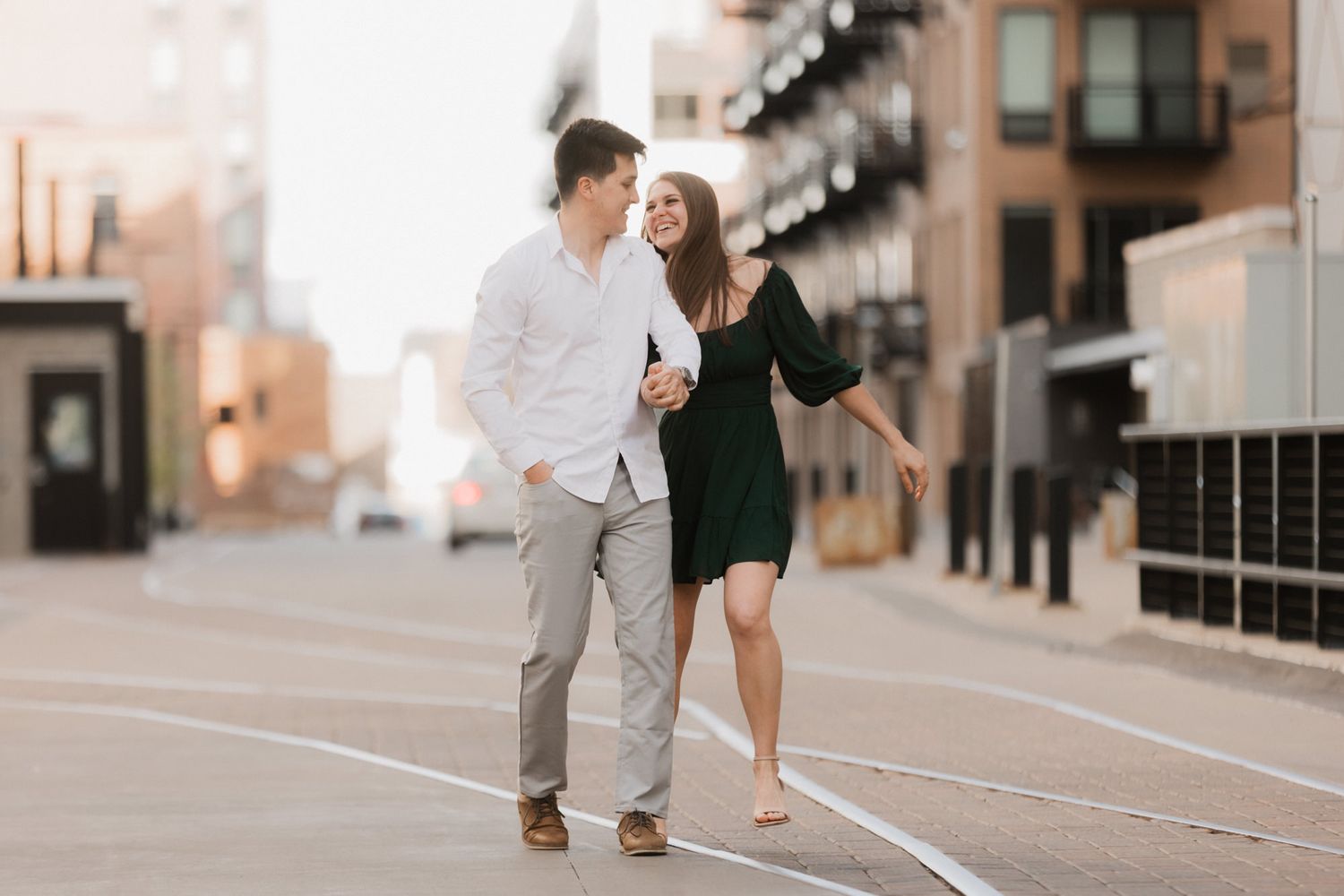 Couple walking together on urban street, woman in green dress holding mans arm while smiling at each other.