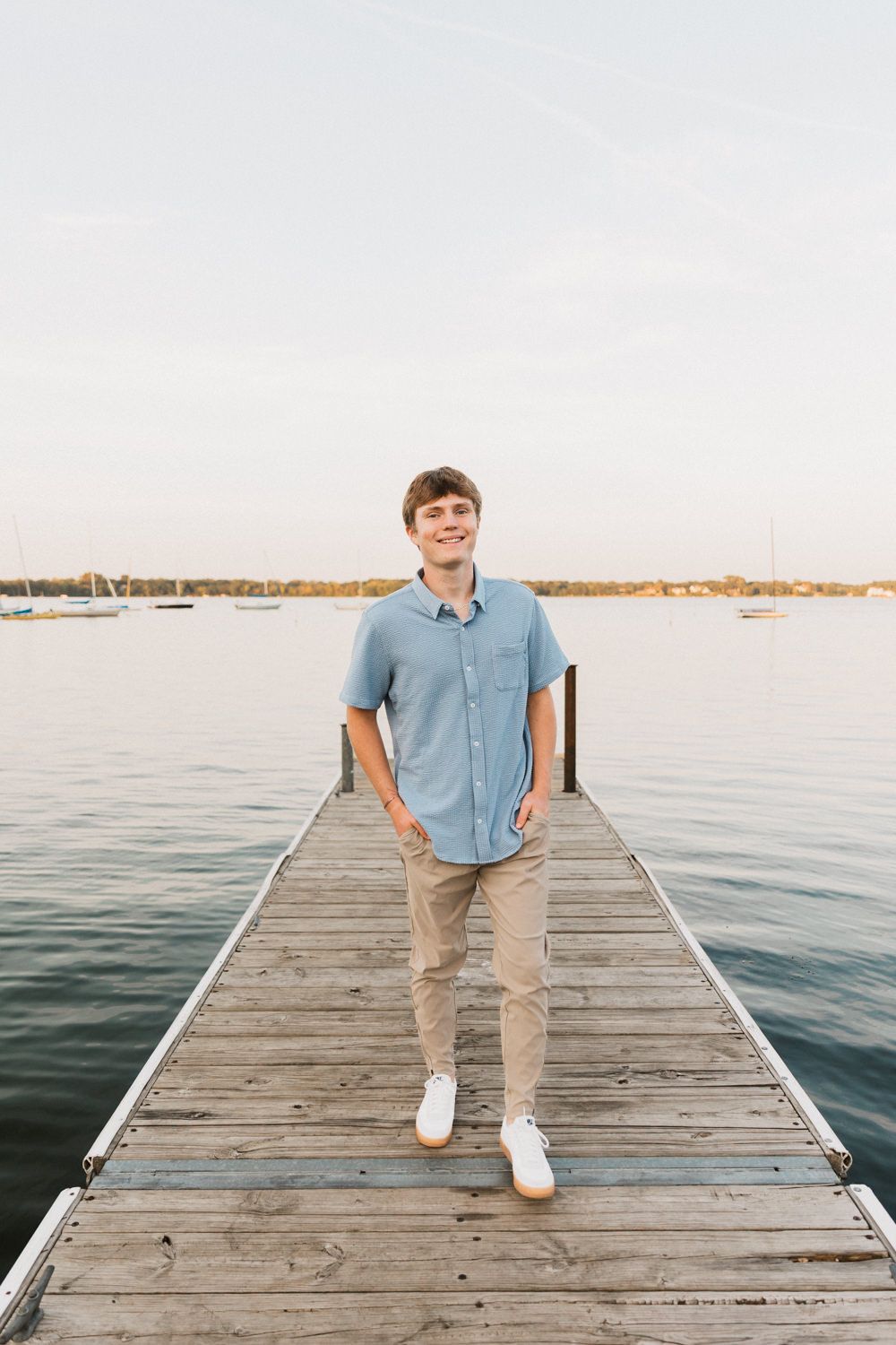 Person in blue shirt standing on wooden dock overlooking calm water at sunset.