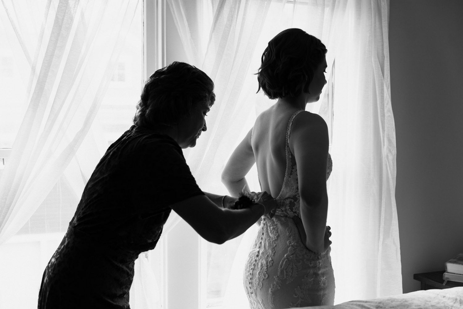 Silhouetted figures against bright window with flowing white curtains in dramatic black and white.