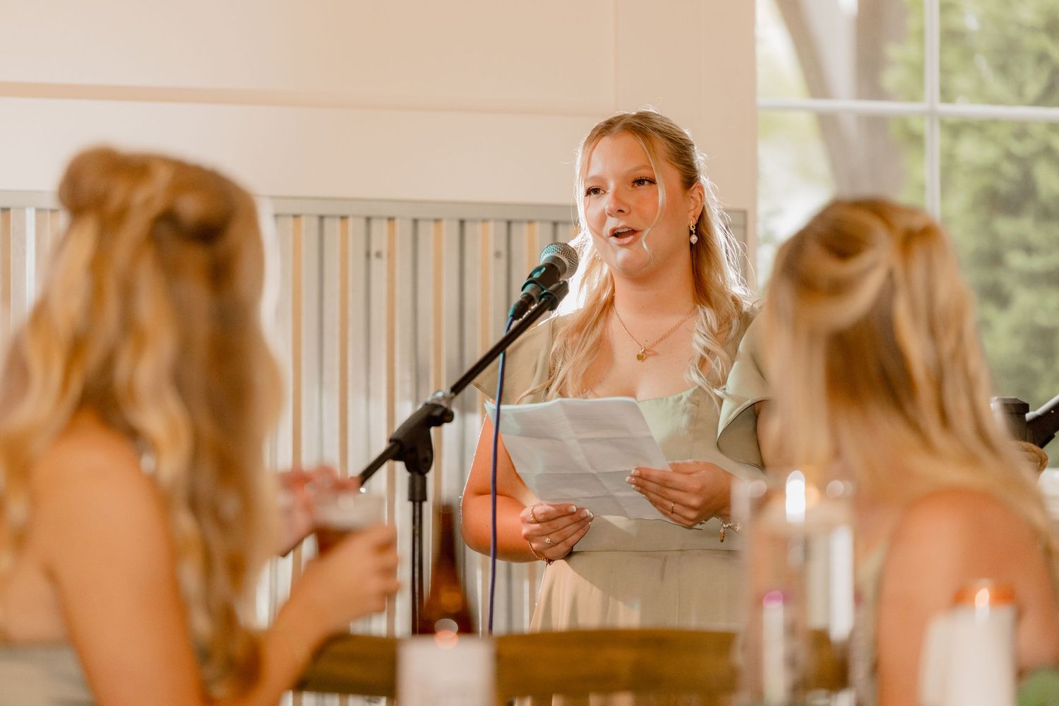 Bridesmaid delivers a heartfelt speech at a wedding reception while holding papers near a microphone.