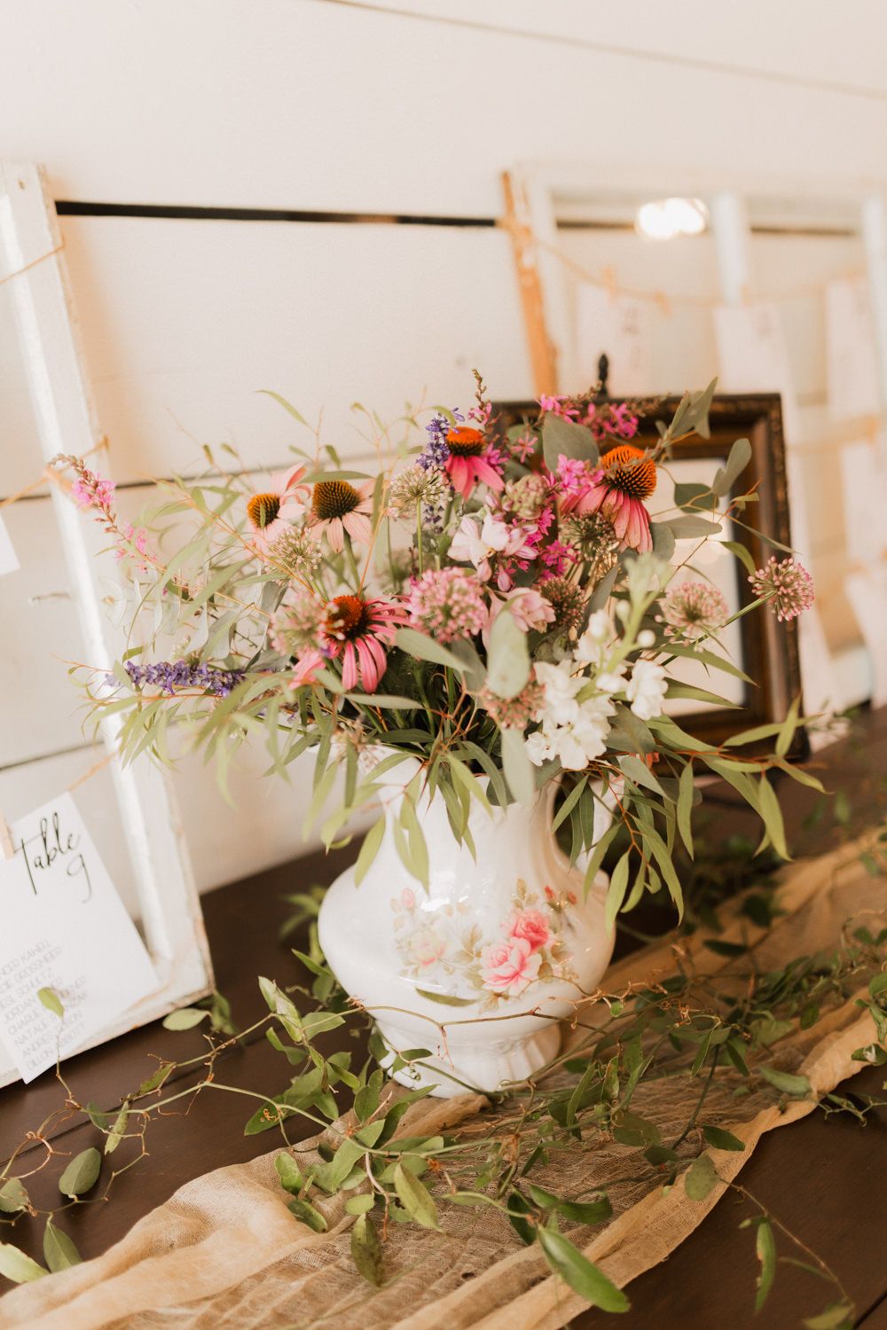 Elegant floral centerpieces with pink and white flowers arranged in white vases on a rustic wooden table.