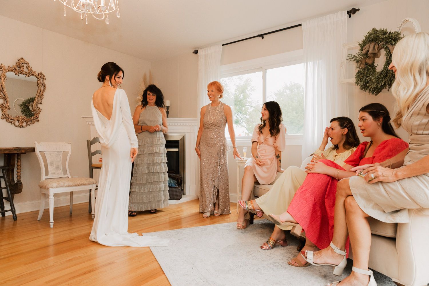 A group of people in formal attire gather in an elegant room with white walls and hardwood floors for a special occasion.