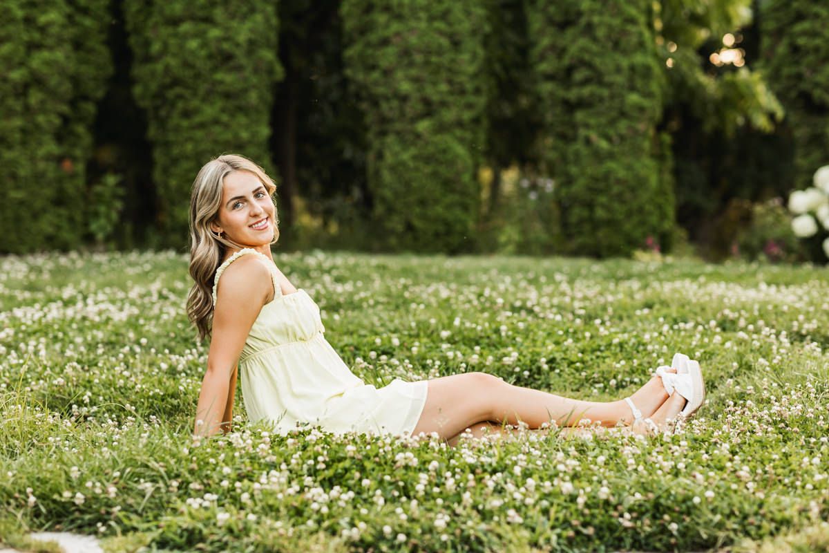 Outdoor portrait session in a garden with flowering ground cover and tall evergreen trees in the background.