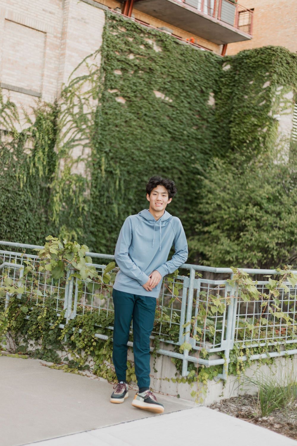 A person wearing a light blue sweater and jeans sits casually on a metal railing in a garden setting.