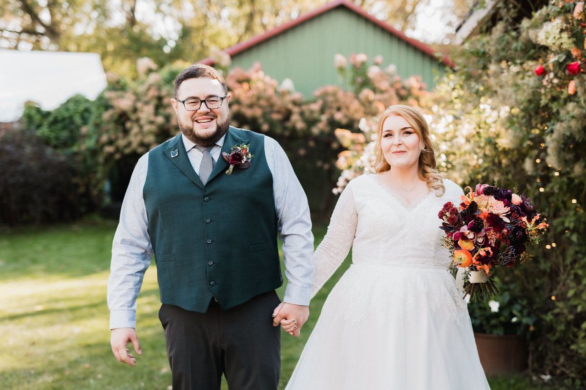A couple shares a joyful moment during their autumn wedding celebration in a garden setting.