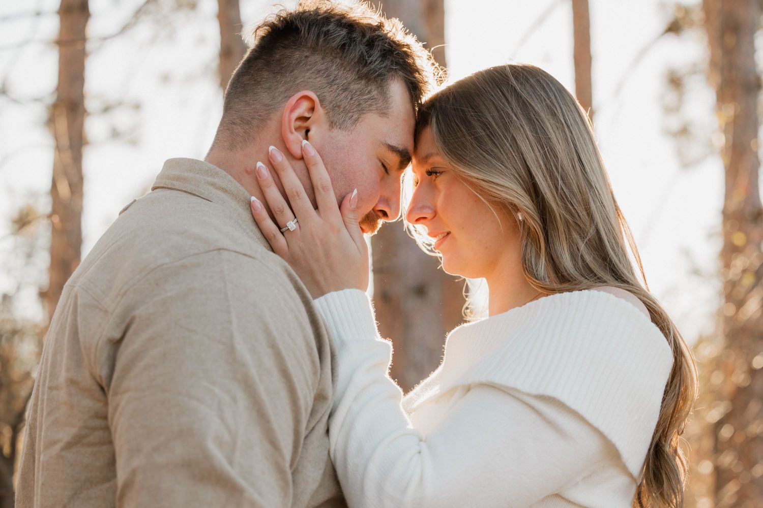 A romantic couple embraces in a sunlit forest during a golden hour engagement photo session.