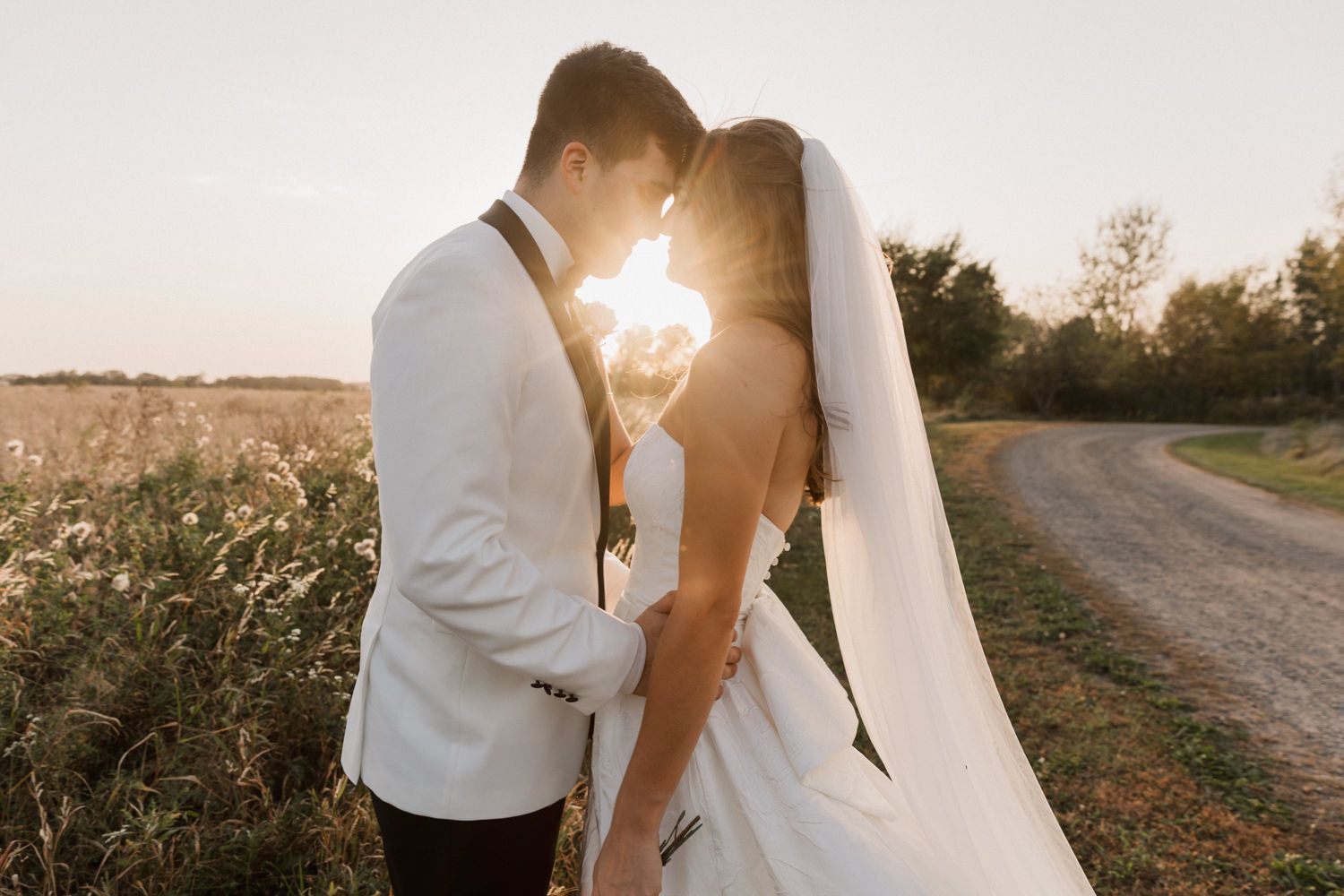 Newlyweds pose along country road during golden hour with dramatic veil movement.