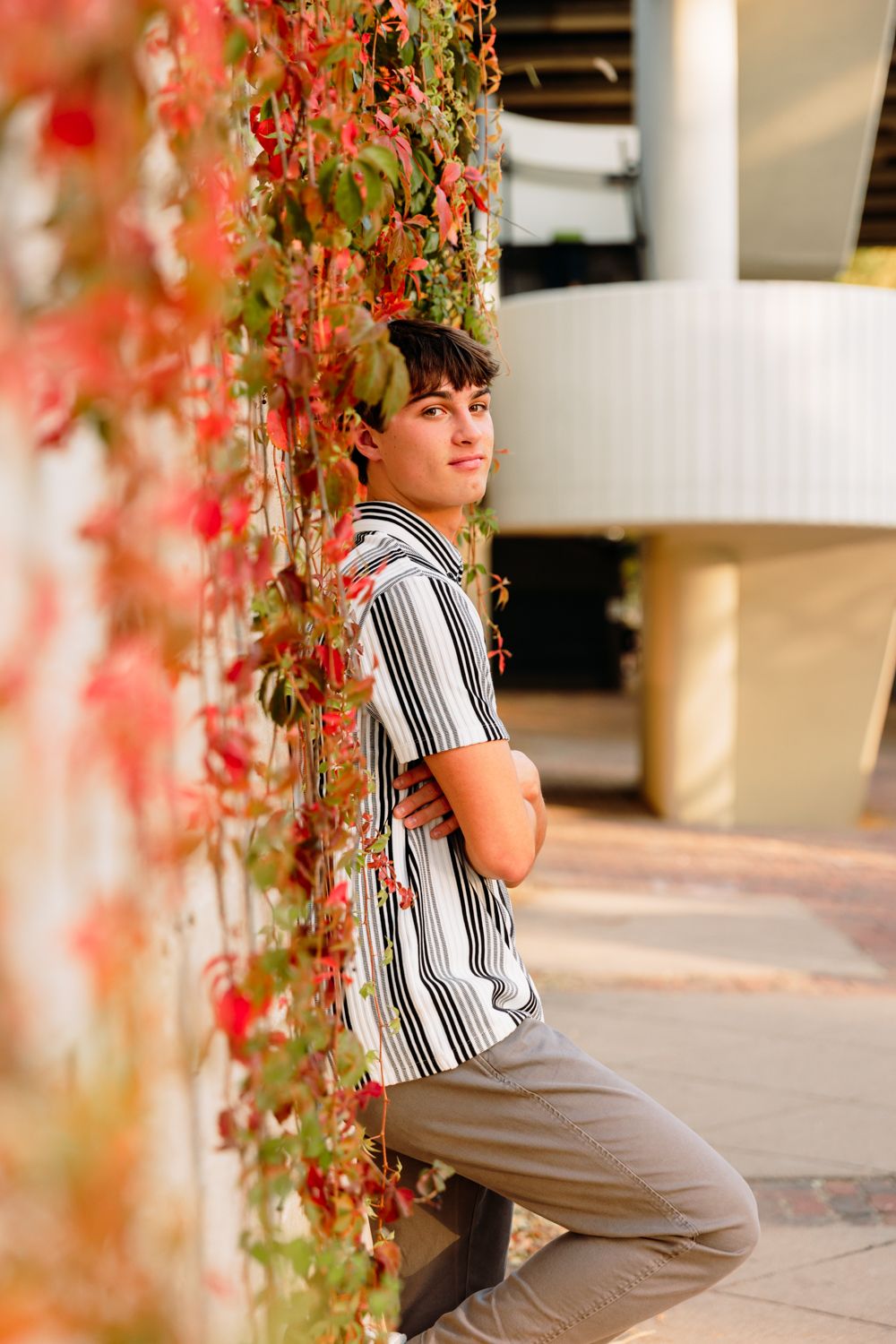 A person in a striped polo relaxes near coral-colored leaves in an outdoor setting.