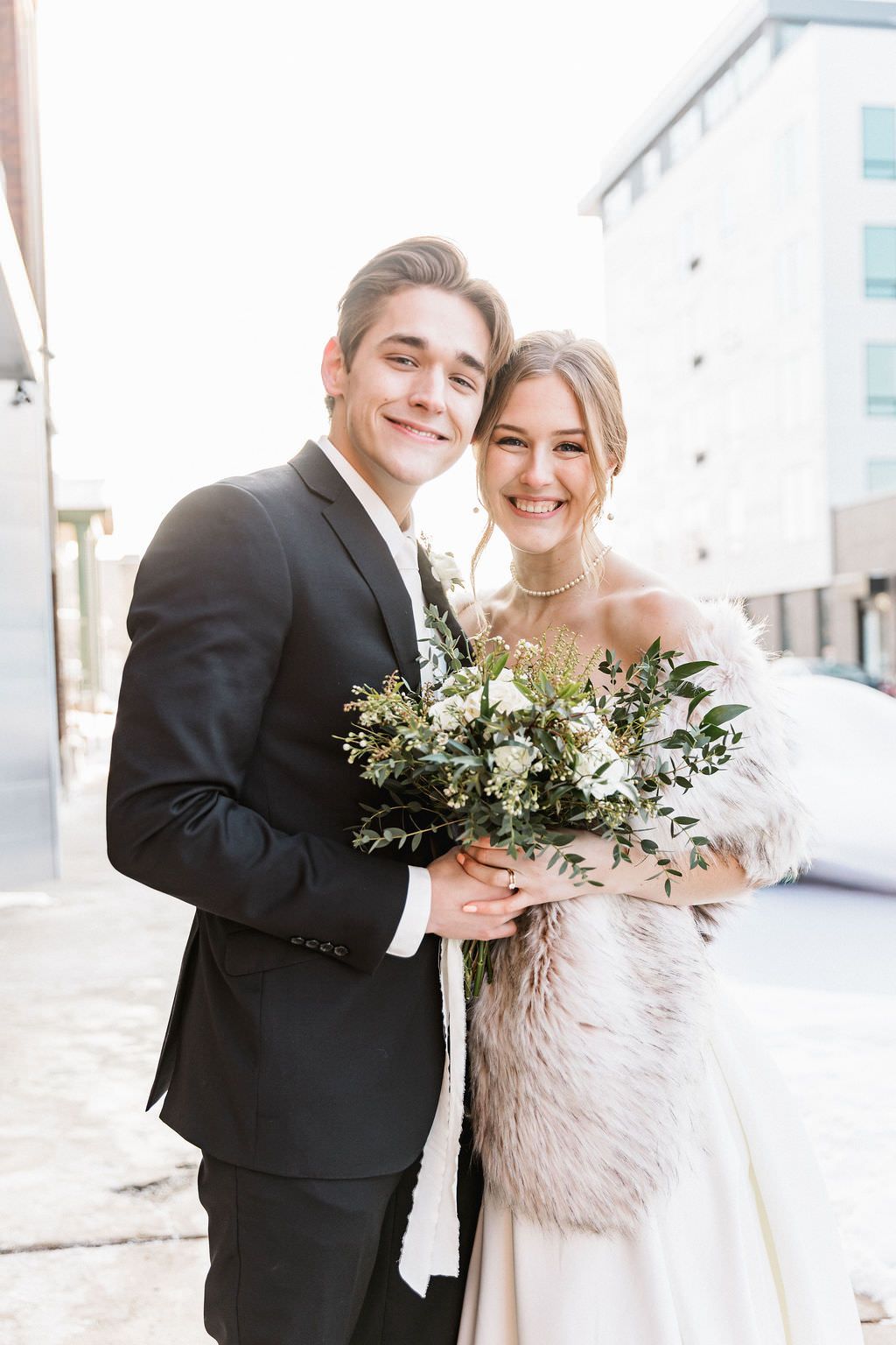 A winter wedding couple poses outdoors while wearing elegant attire with a fur wrap.