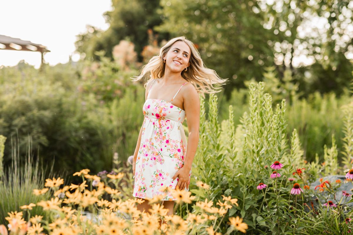 A floral summer scene with someone wearing a floral print dress amidst colorful blooming flowers and greenery.