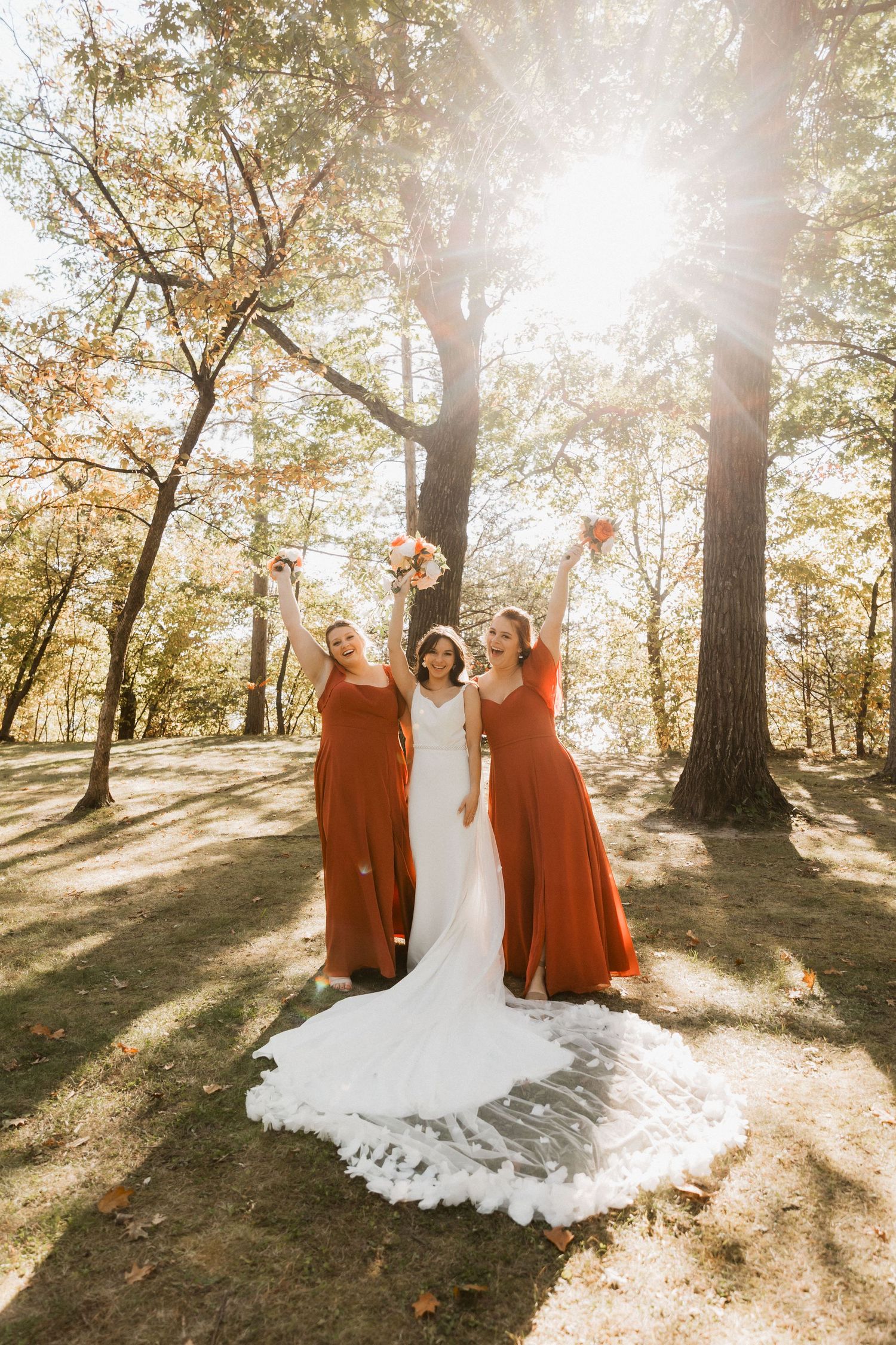 Bridal party poses in autumn forest with sunlight streaming through trees creating magical golden lighting effect.