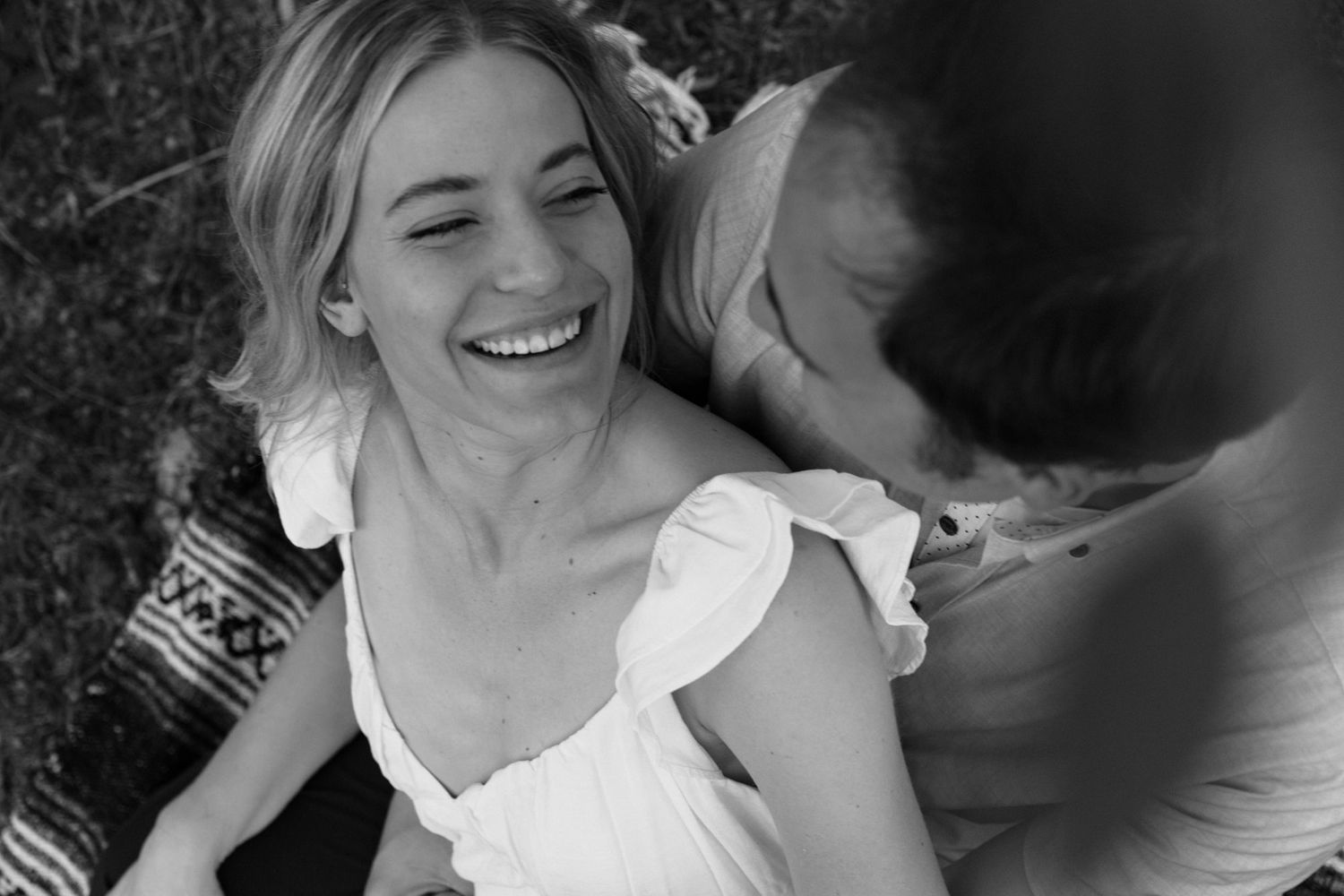 Black and white photo of a laughing blonde woman in a white dress enjoying a sunny outdoor picnic.