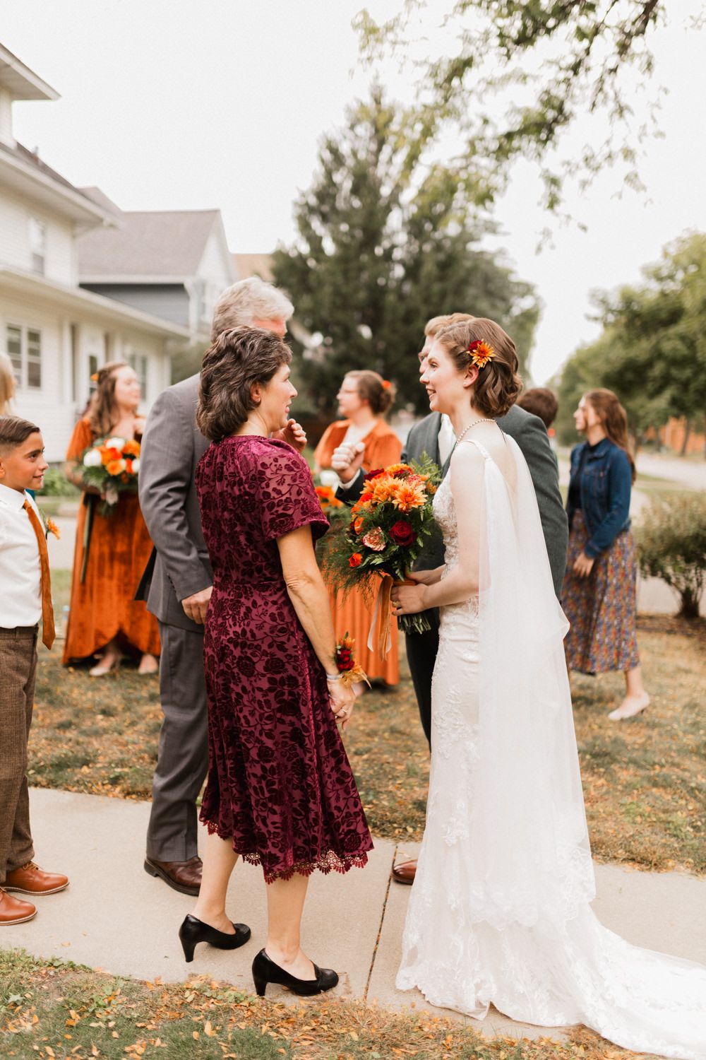Wedding party dances in a line outdoors wearing burgundy and orange fall colors with white bridal gown.