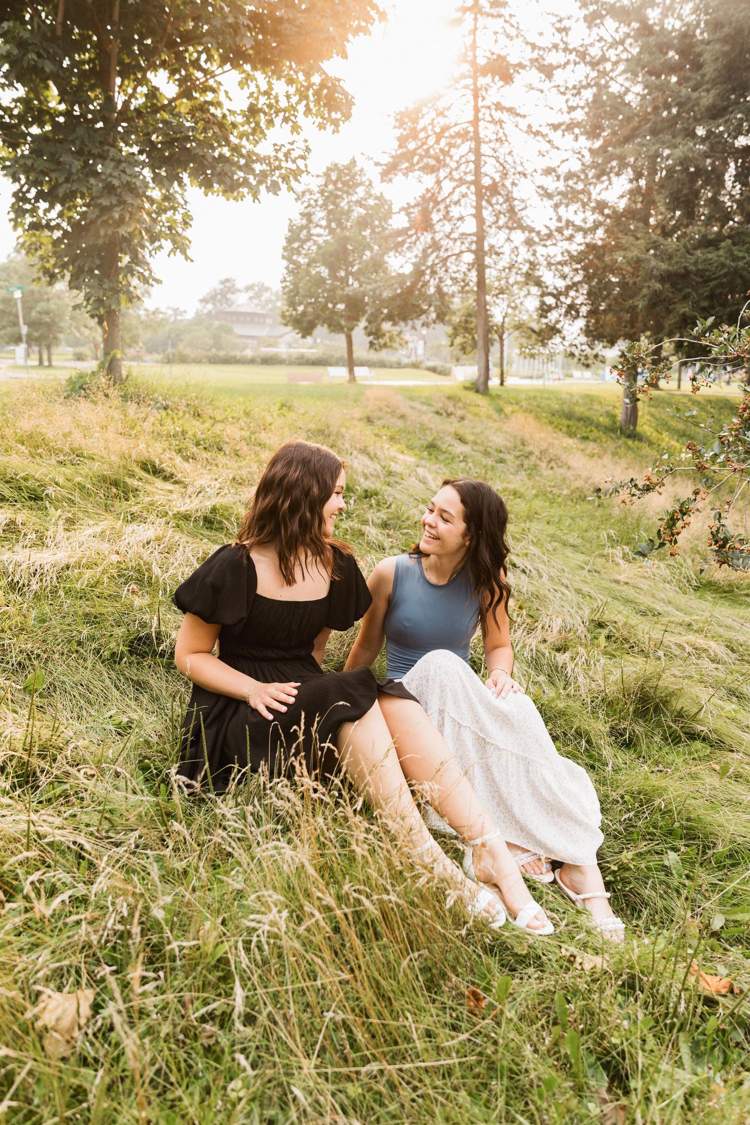 Two friends share a joyful moment together while sitting in tall grass during golden hour.
