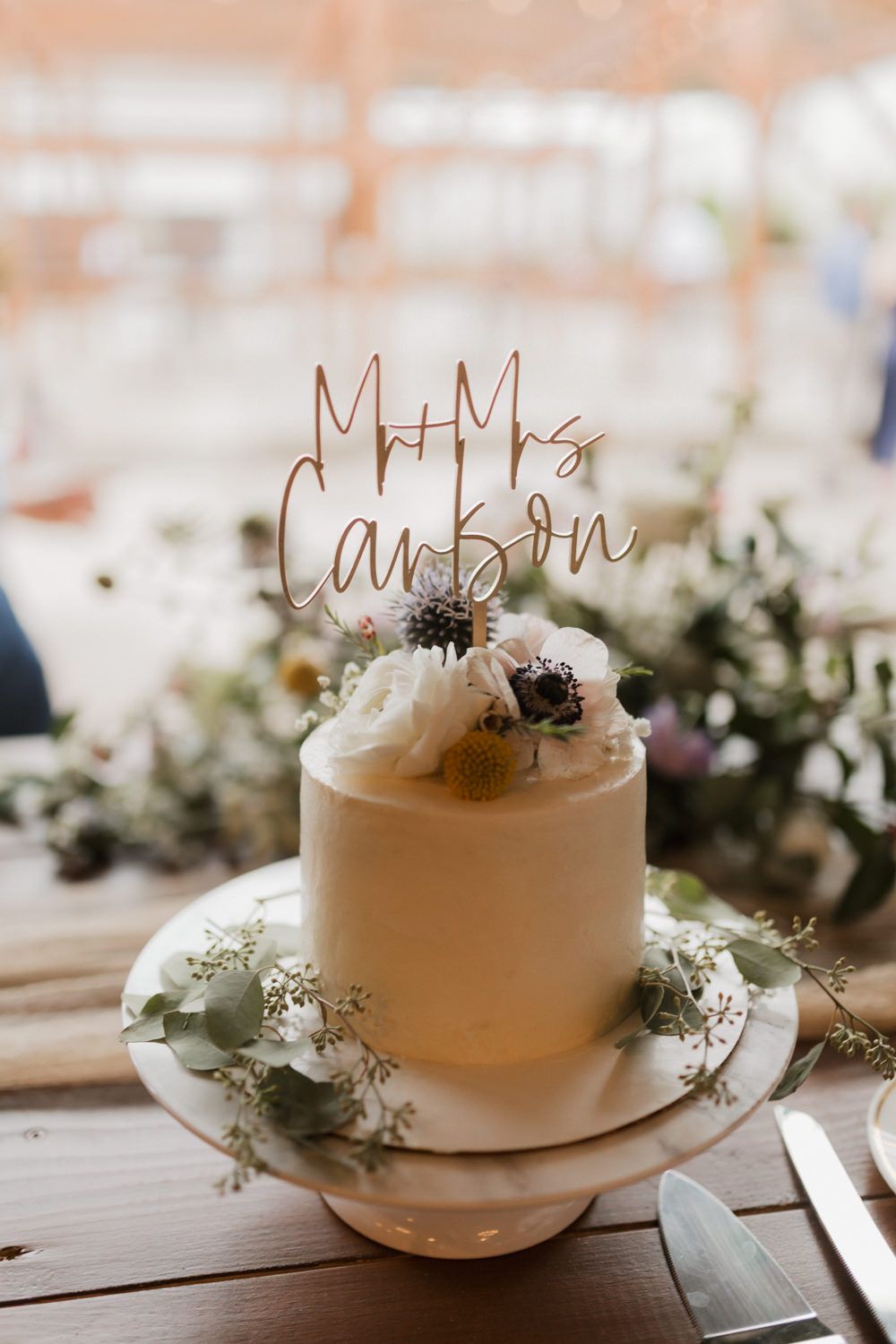 White wedding cakes displayed on wooden tables with floral decorations and rustic name toppers.