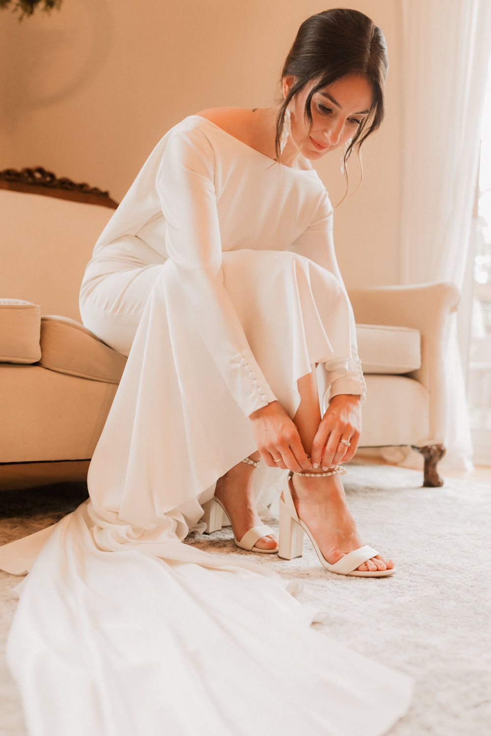 Person in white dress sitting cross-legged on beige carpet in warm, naturally lit interior.