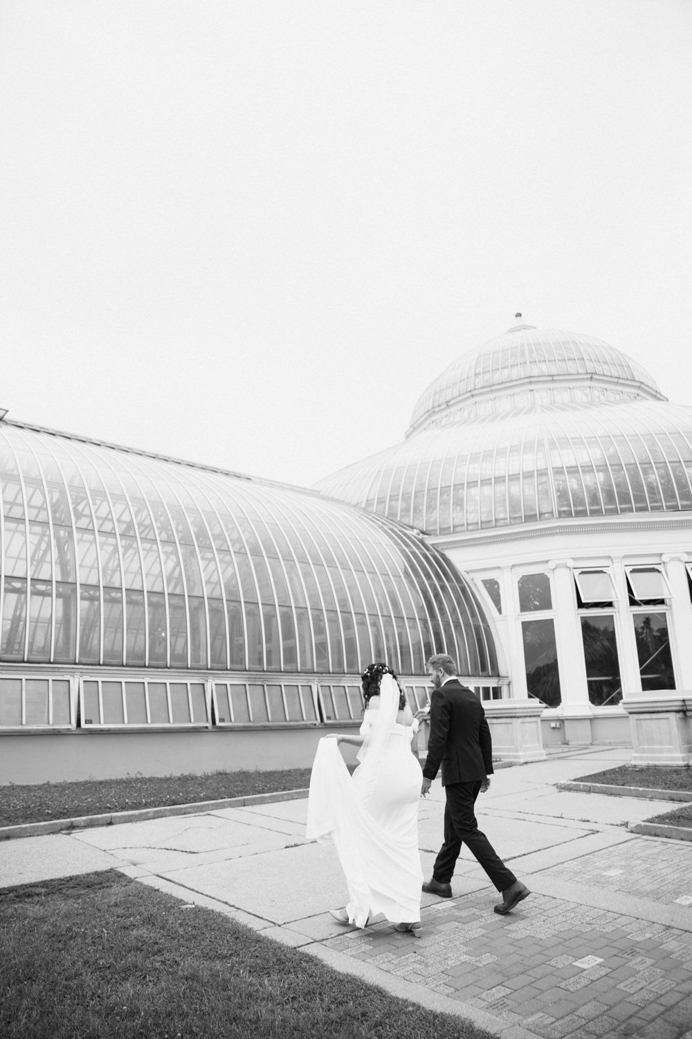 Black and white photo series of a couple walking in front of a magnificent glass greenhouse structure.