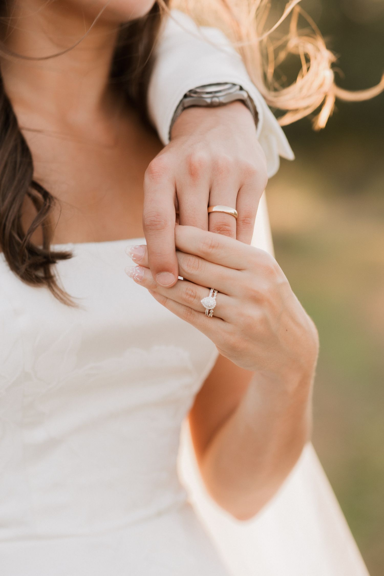 Close-up of bride and groom holding hands, showcasing diamond engagement ring and gold wedding band.