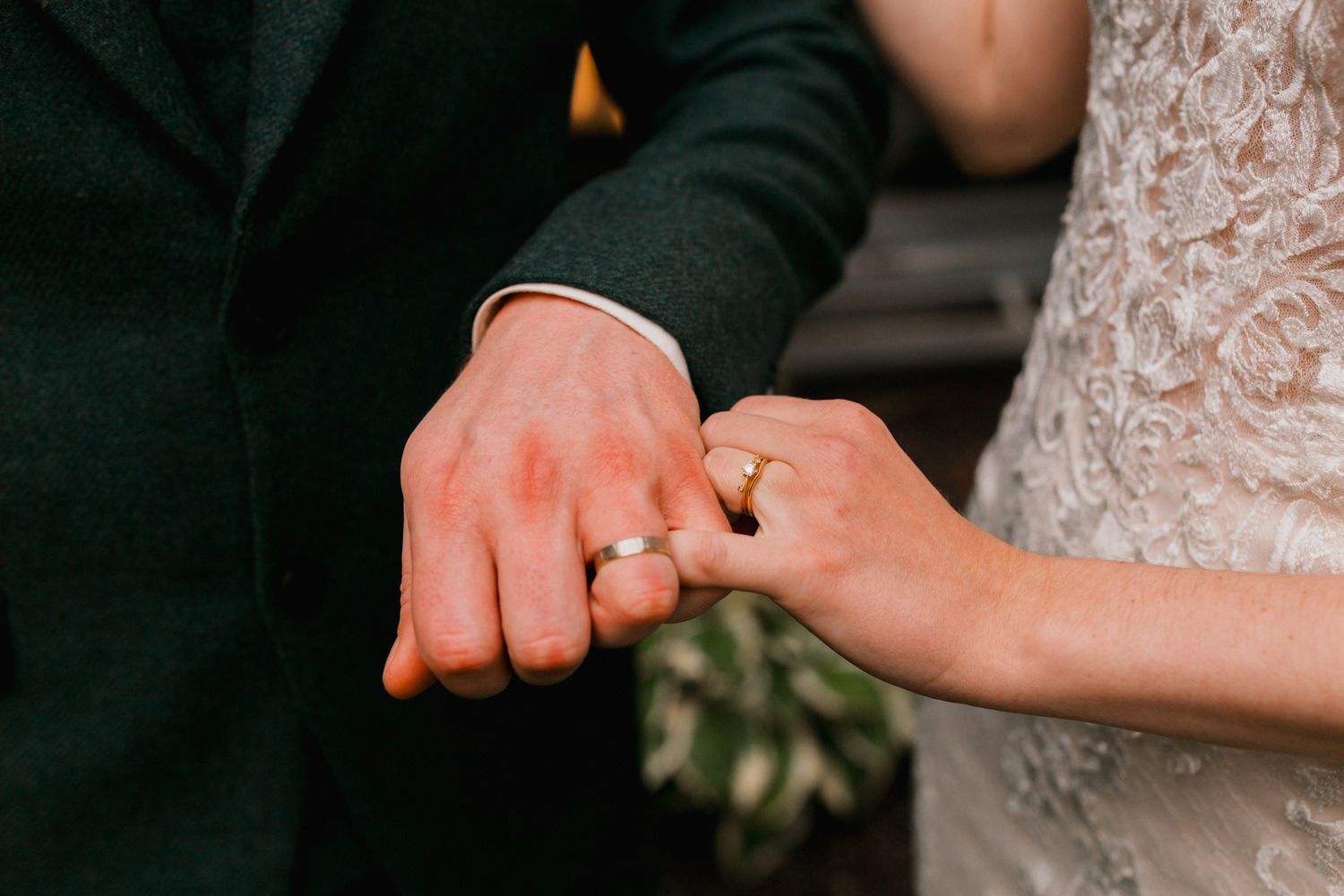 Close up of hands showing wedding rings with floral bouquet in the background.
