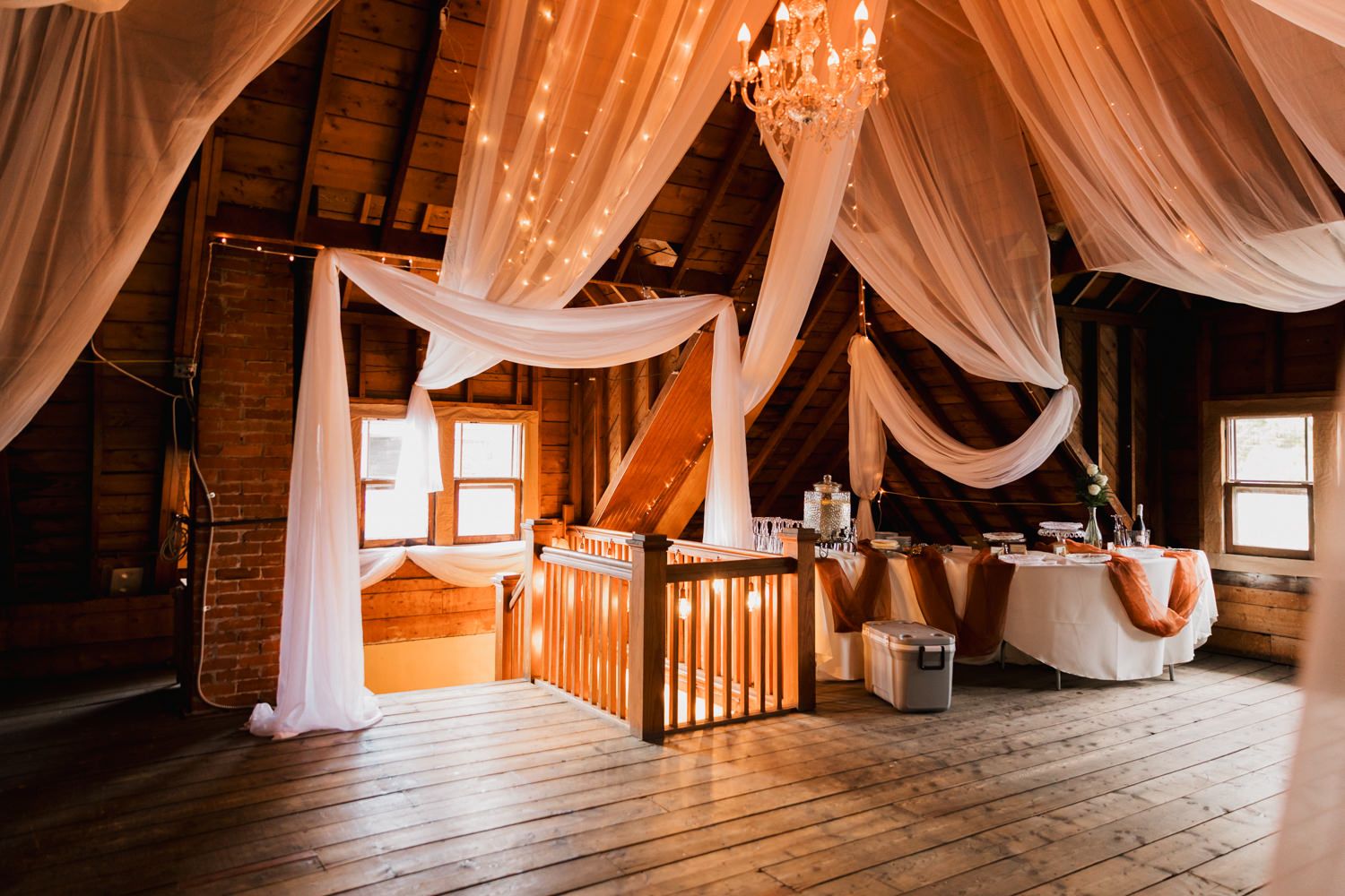 Elegant white fabric drapes create a romantic canopy effect in a rustic wooden attic space.