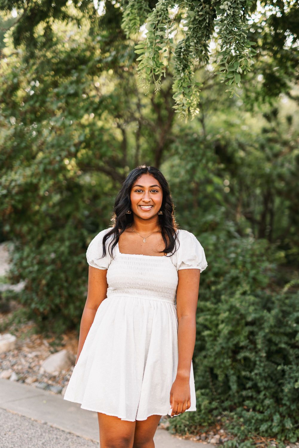 Cheerful outdoor portrait in white dress against green garden background.