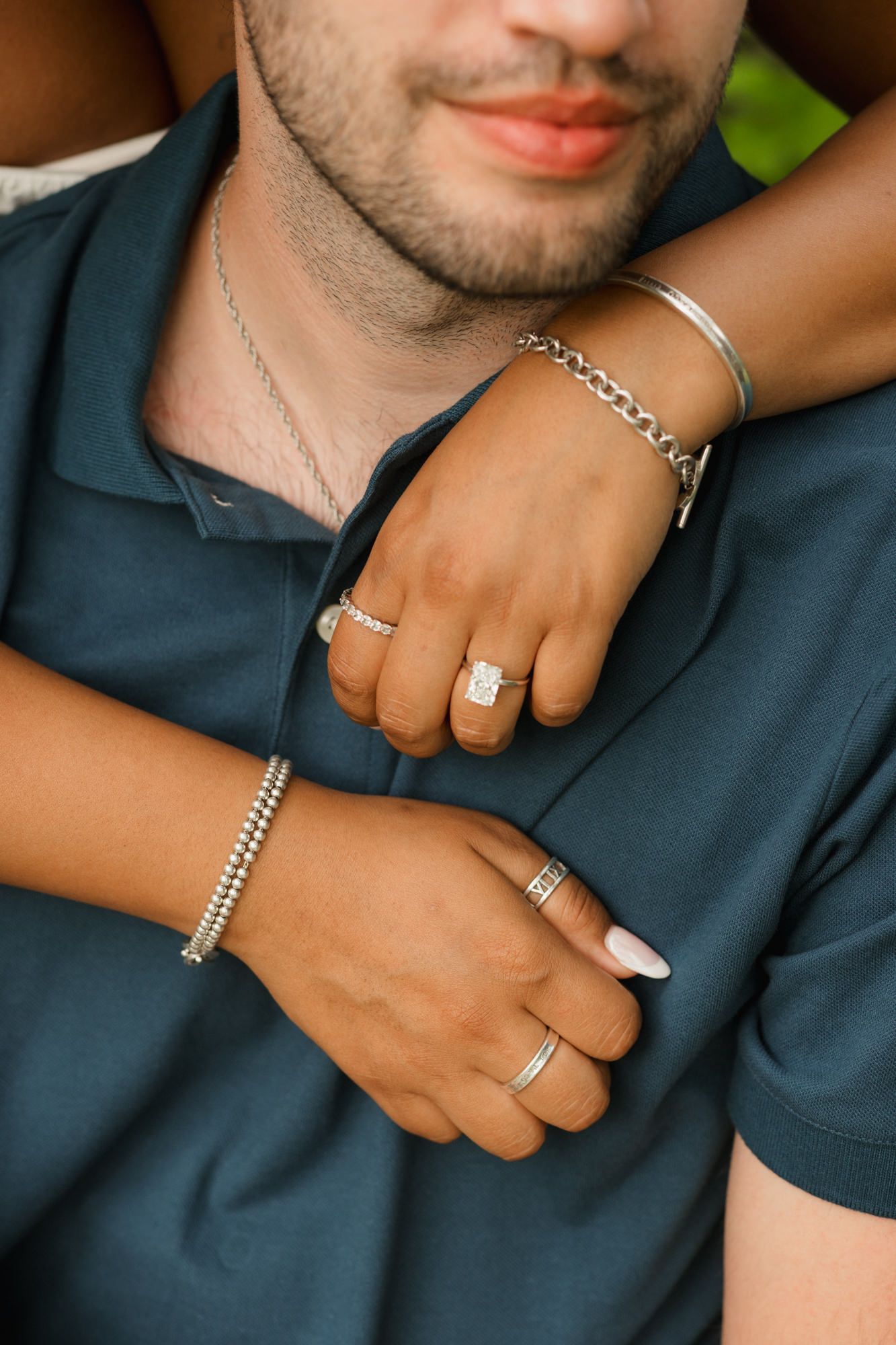 Close-up of a couple's hands showing engagement ring, wedding band, and silver bracelets.