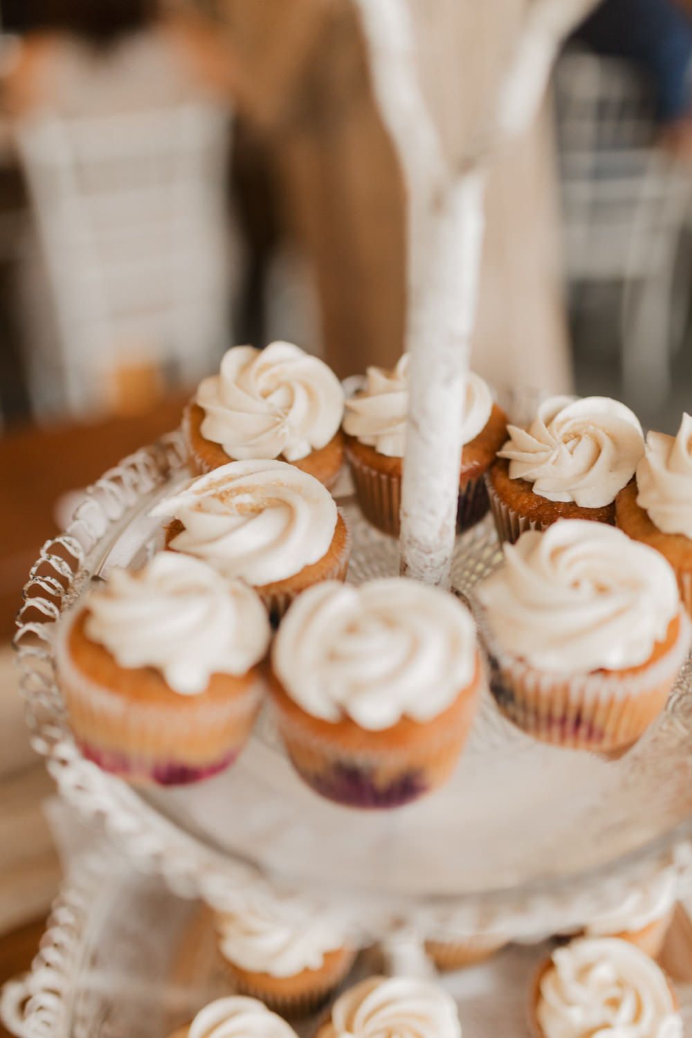 Elegant white frosted cupcakes displayed on a tiered serving stand at a wedding reception.
