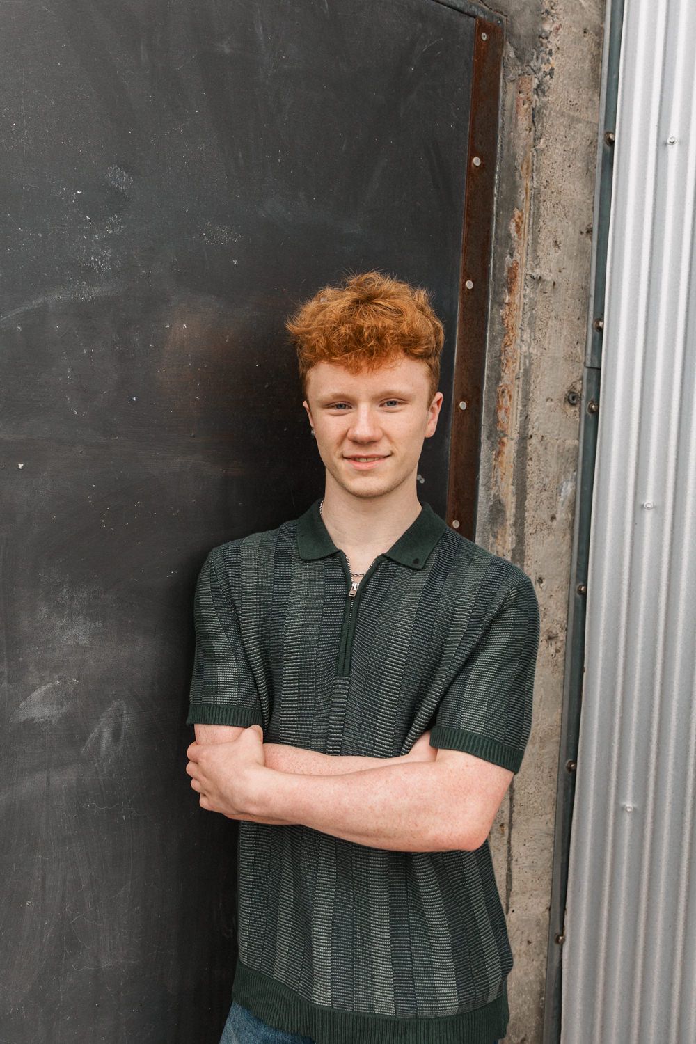 A casual portrait pose against a black door wearing a striped green polo shirt.