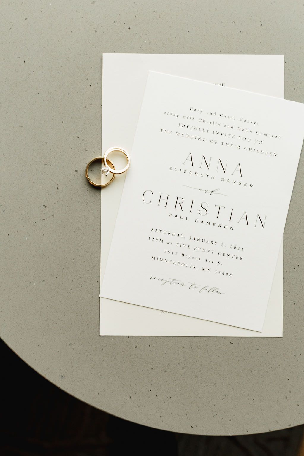 Simple and elegant white wedding invitation cards beautifully arranged with golden rings on a neutral gray background.