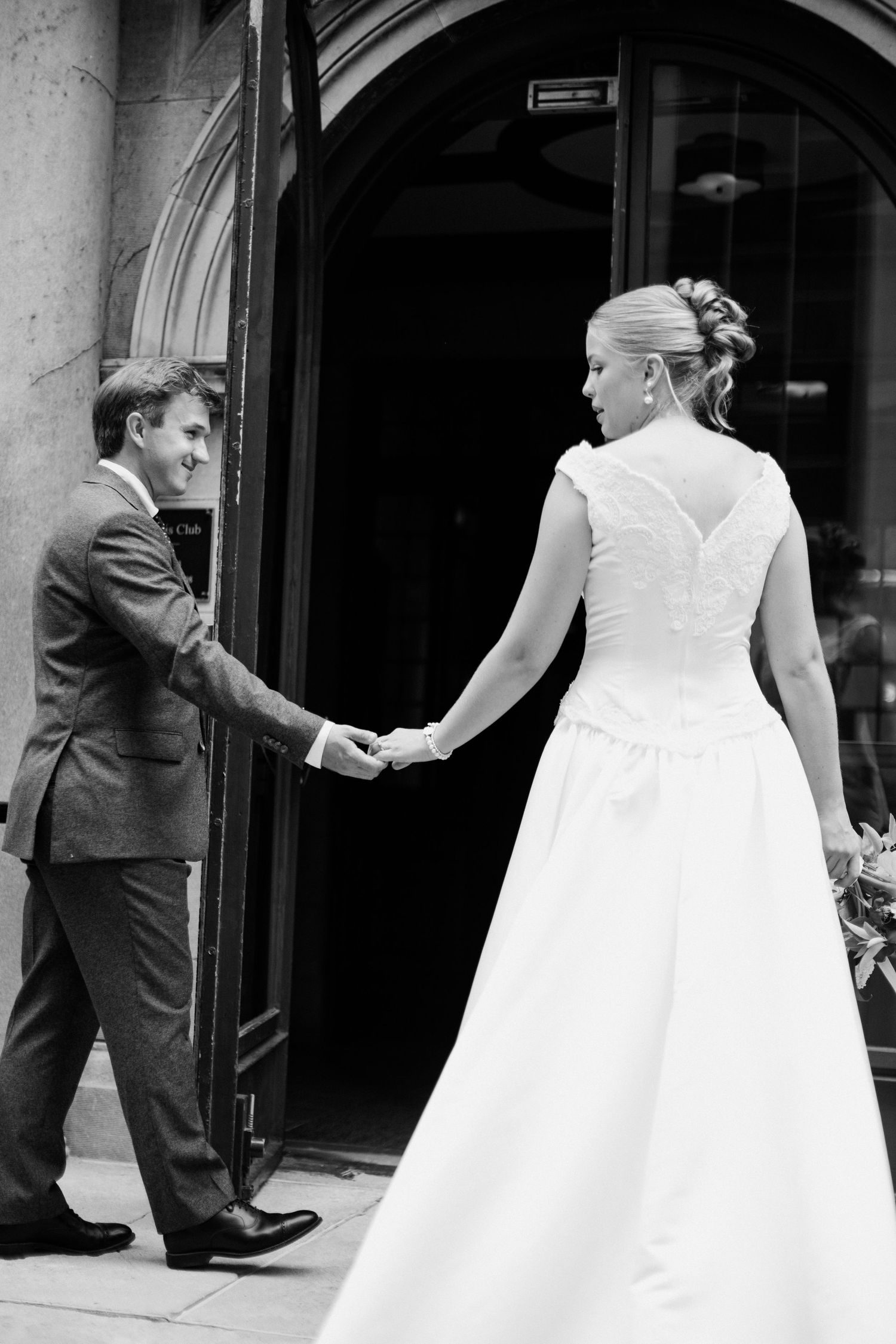 Black and white photo of a bride and groom holding hands at a church entrance on their wedding day.