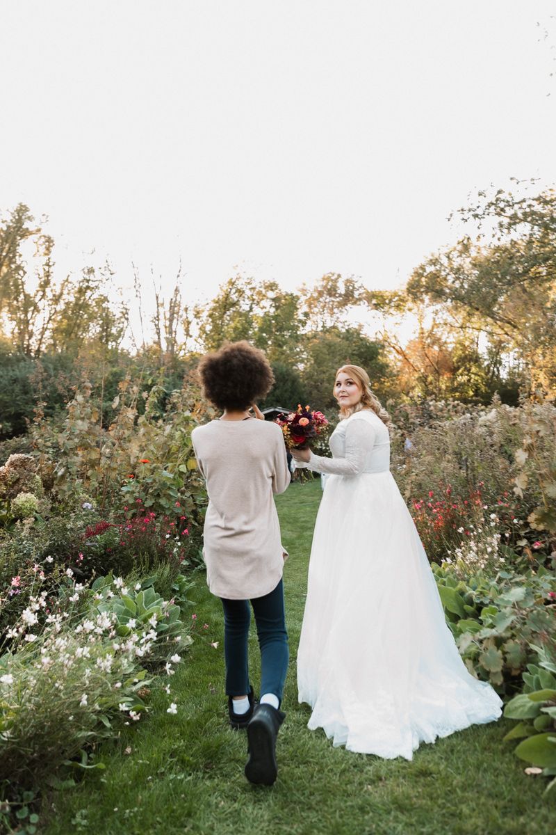 Two people stroll through a romantic garden setting filled with blooming flowers at sunset.