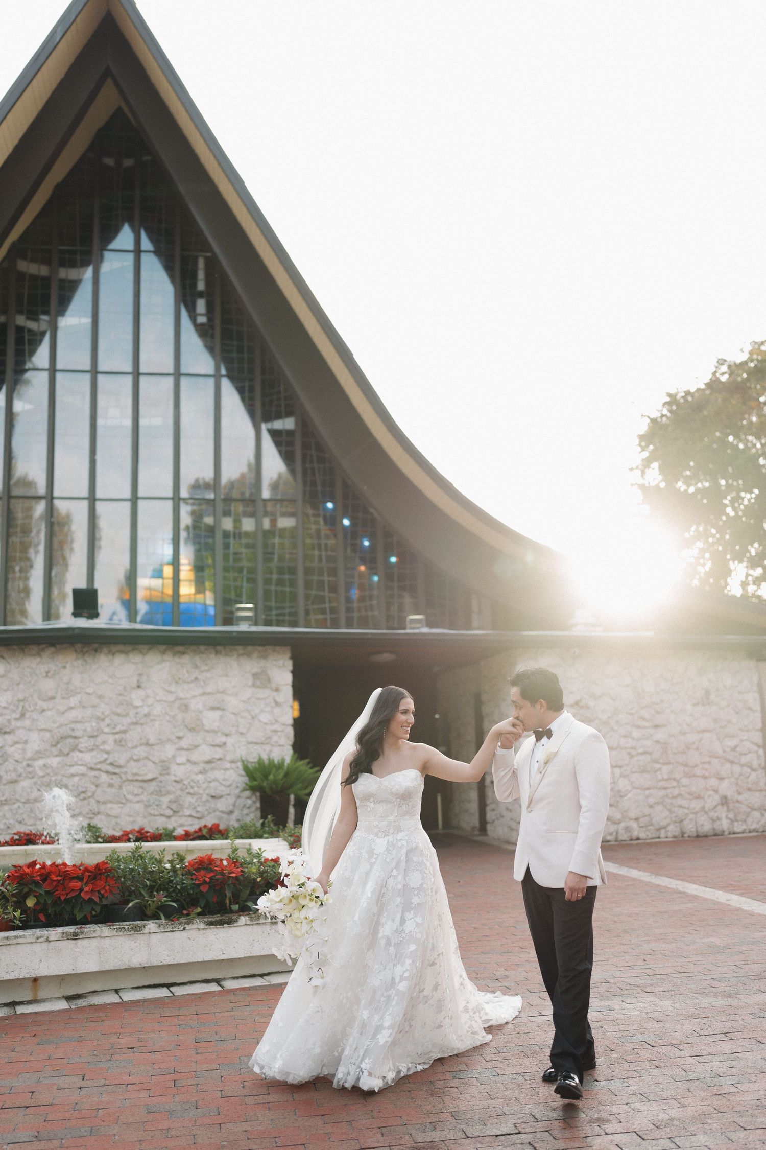 A couple dances in front of a modern church building with floor-to-ceiling windows at sunset.